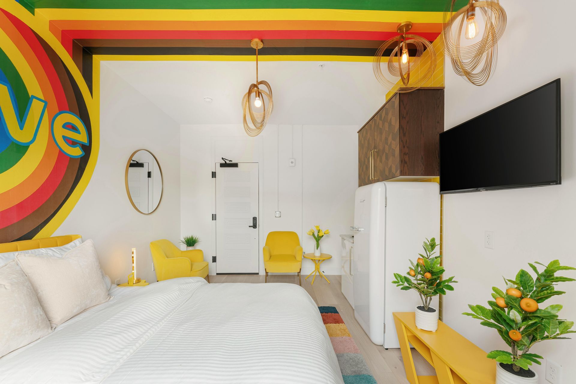 Bright bedroom with white bed, yellow accents, wall TV, and potted plants
