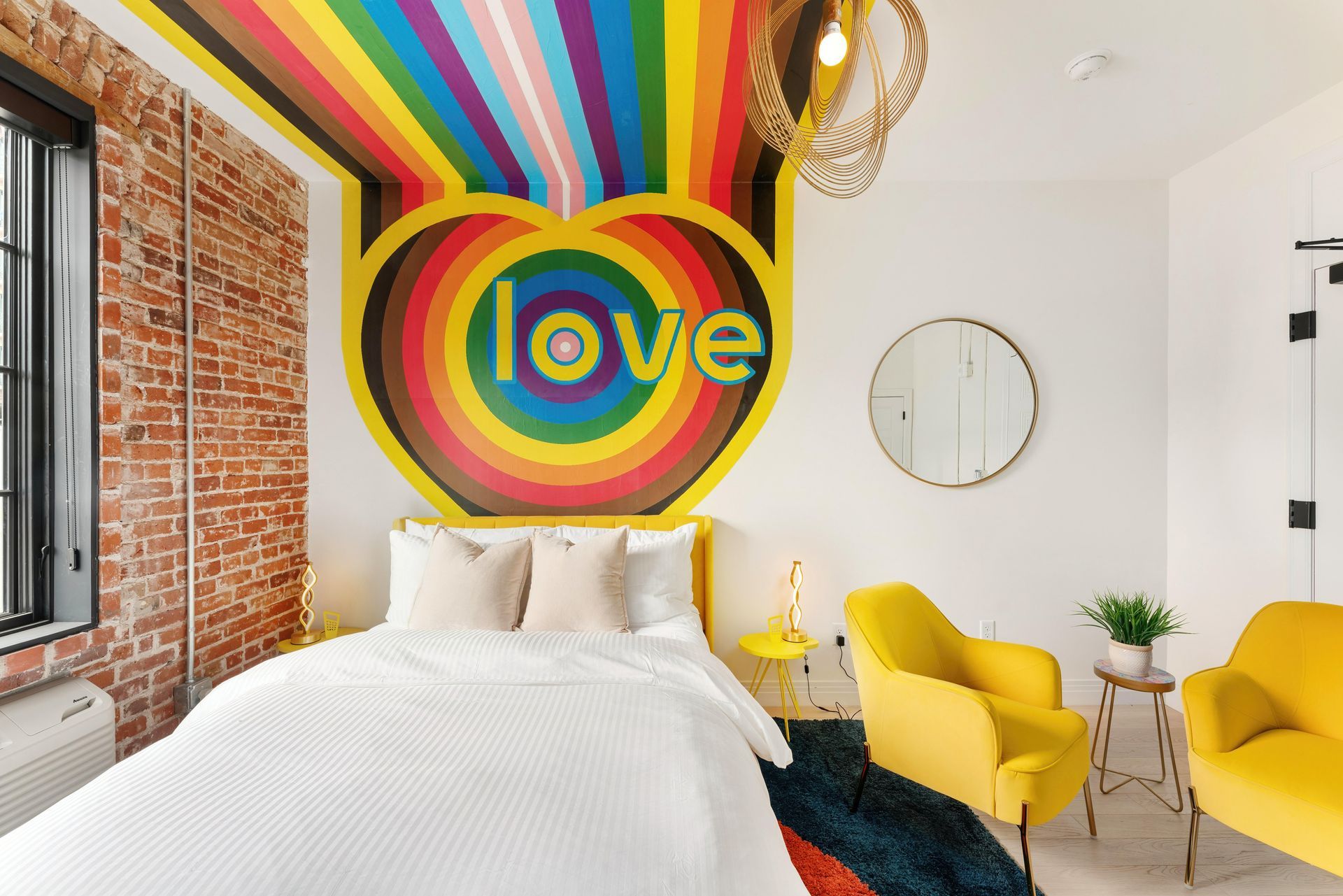 Colorful bedroom with rainbow “love” mural, white bed, yellow chairs, and a round wall mirror