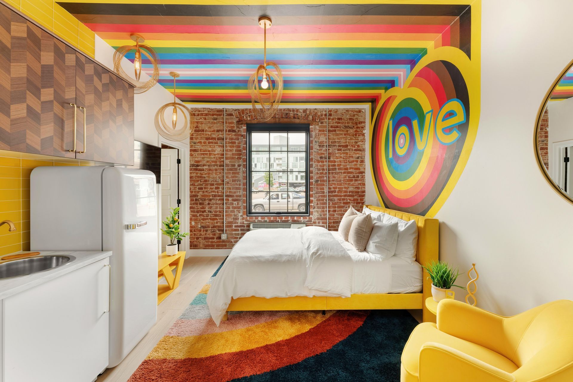 Colorful retro-style bedroom with rainbow ceiling, brick wall, white bed, yellow chair, and heart wall art