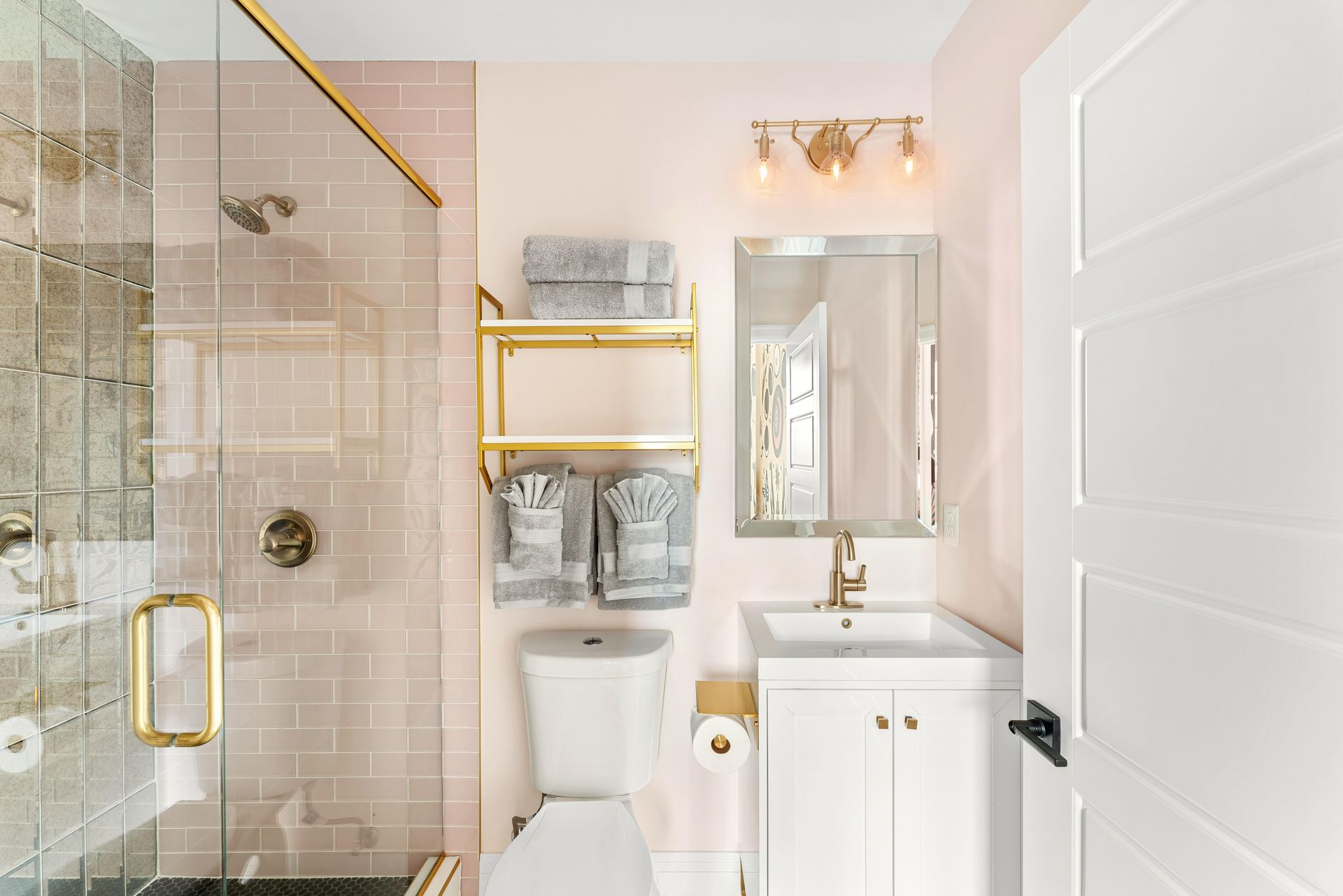 Bright bathroom with glass shower, gold accents, vanity, mirror, and toilet