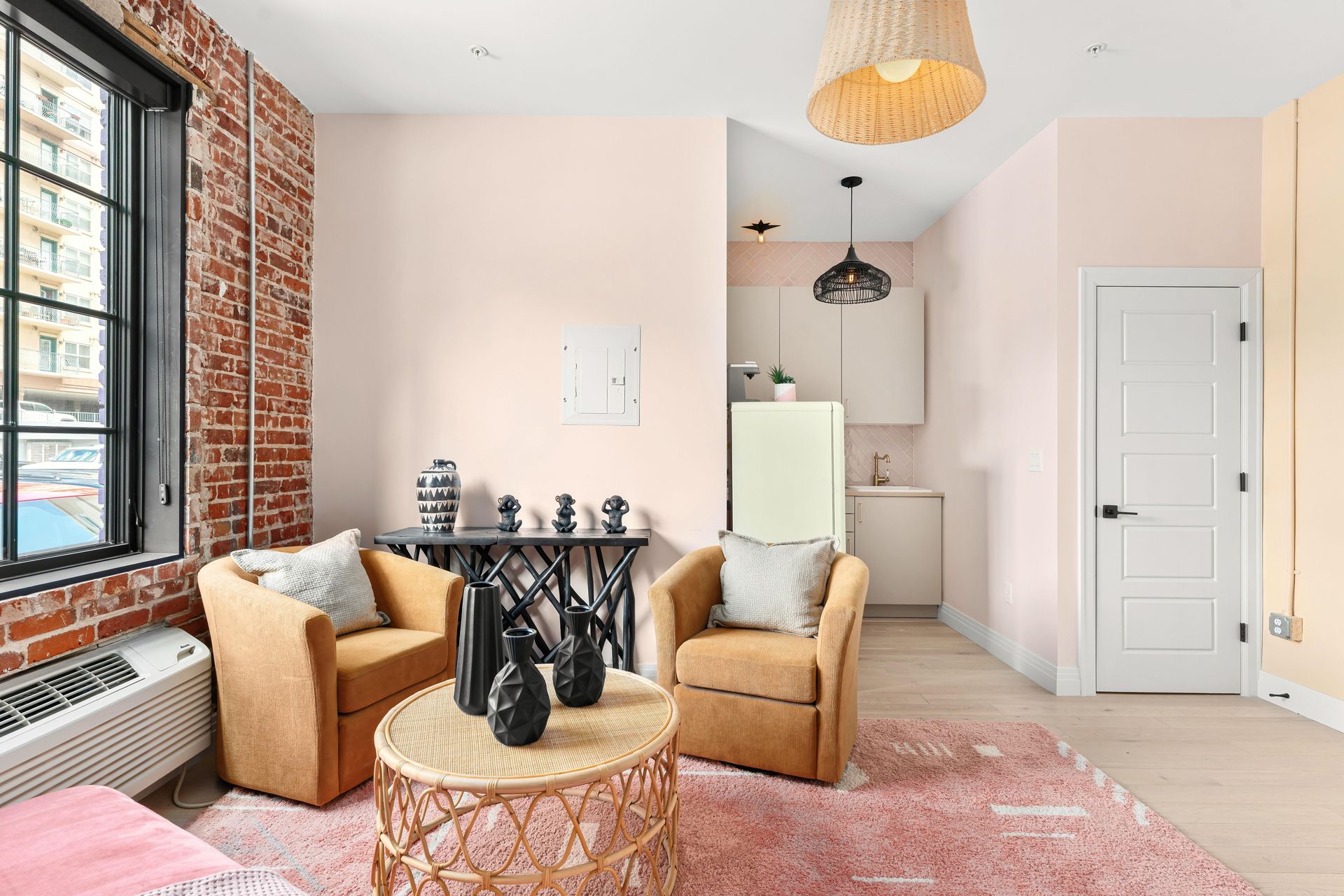 Bright pink bedroom with brick accent wall, large windows, cozy chairs, and a white door.