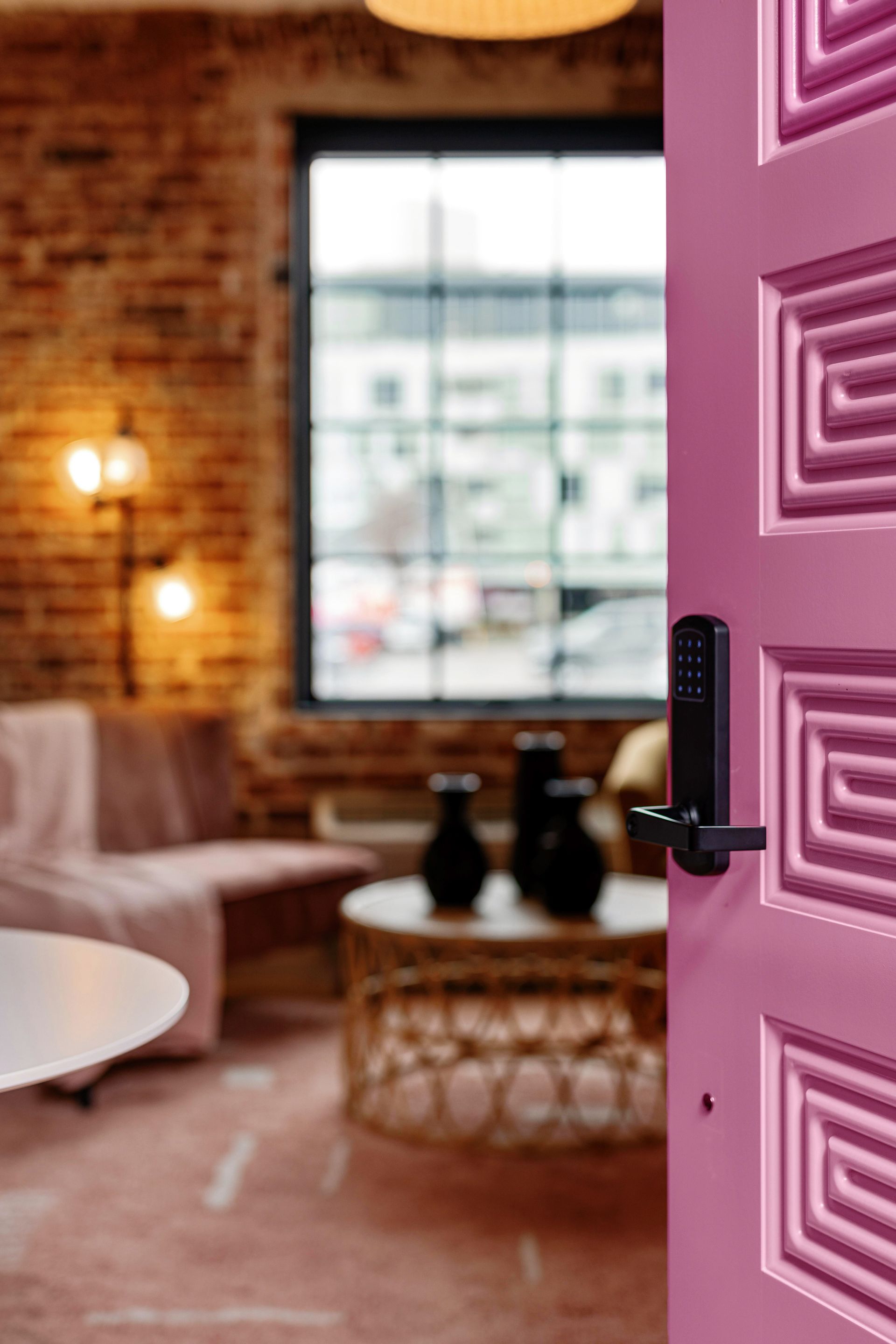 Open pink door revealing a cozy living room with brick walls, window, and warm lighting