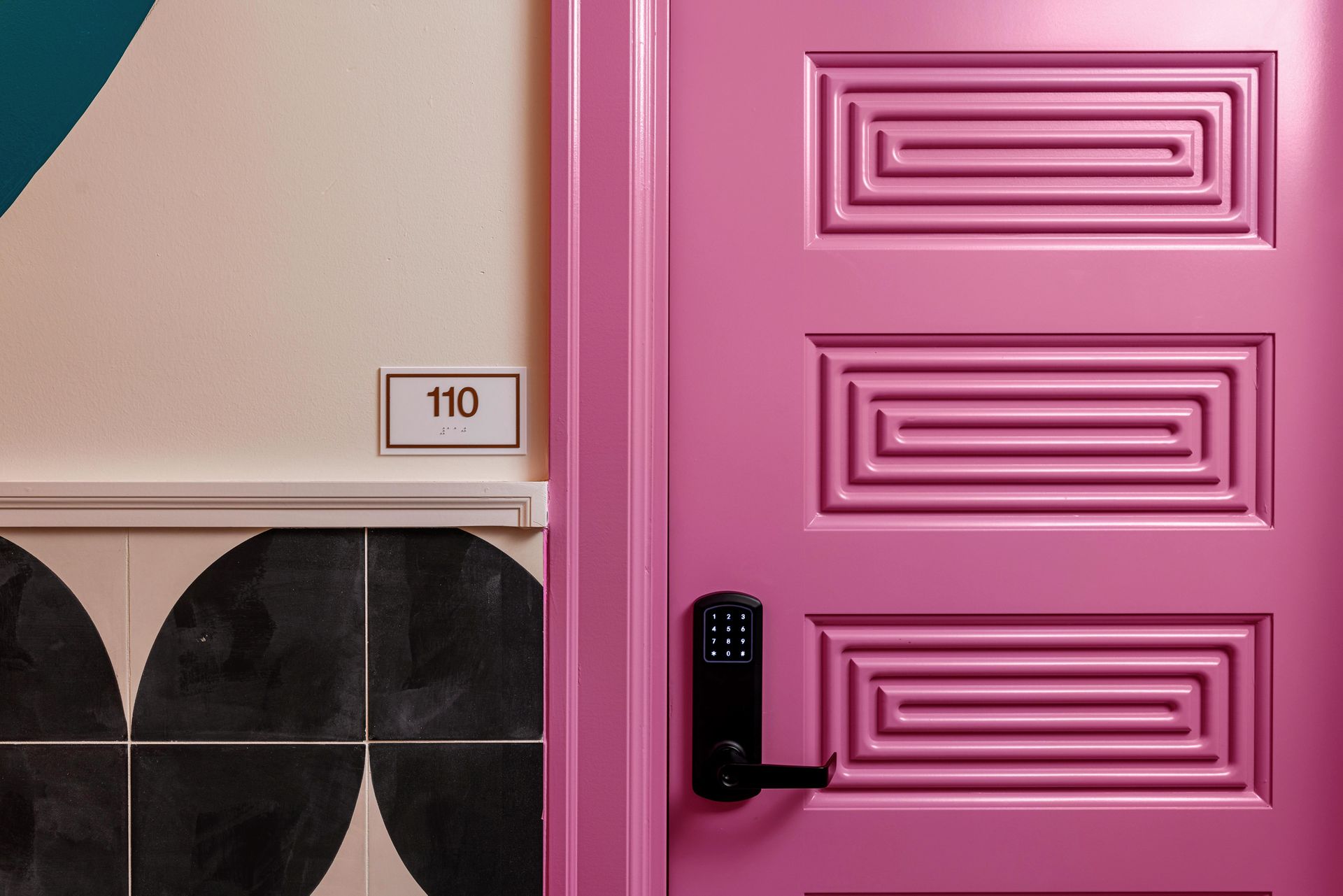 Pink door with black handle beside a beige wall and house number 110