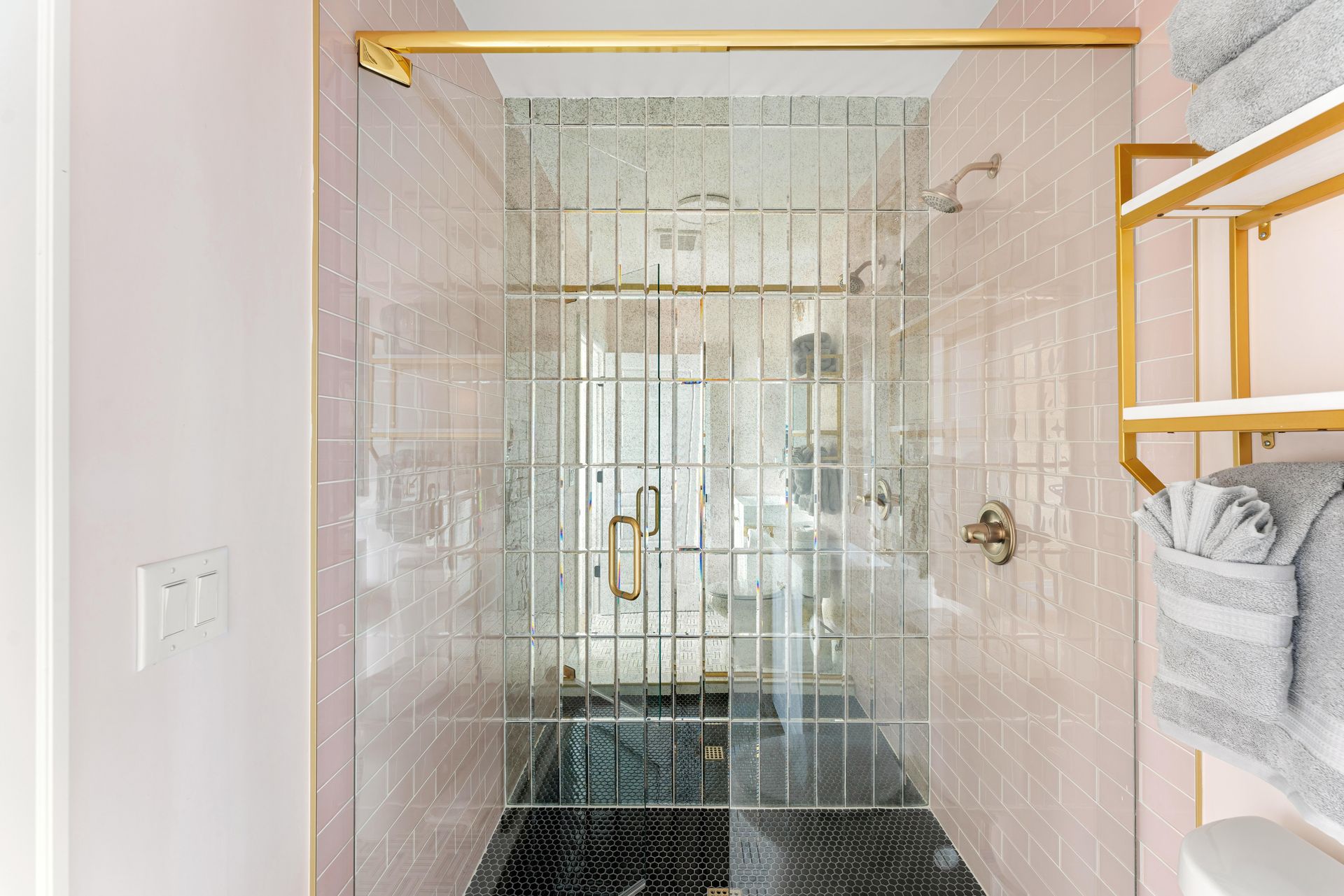 Glass shower stall with gold fixtures in a white bathroom