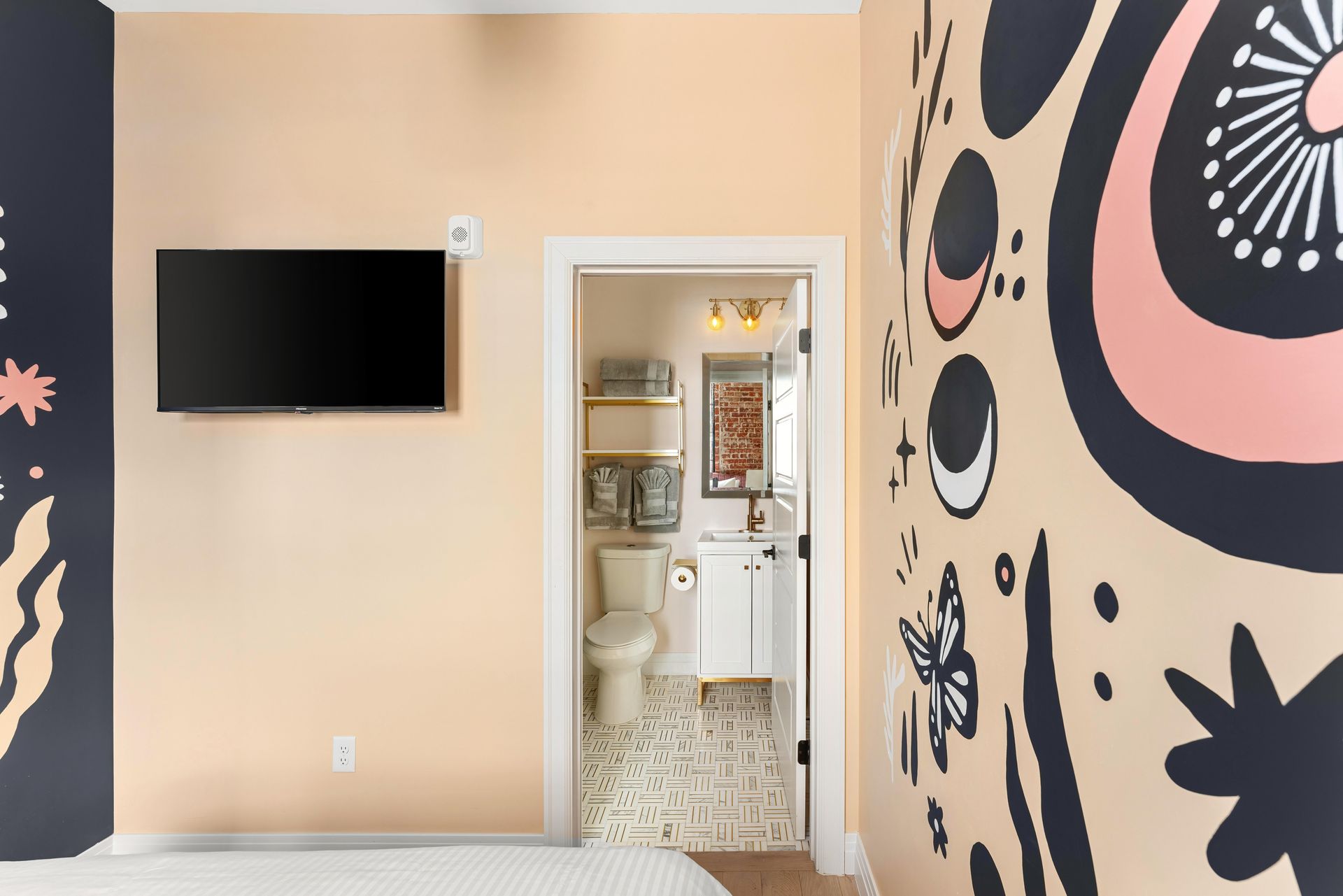 Colorful hallway with mural walls, a wall-mounted TV, and an open doorway to a tiled room.