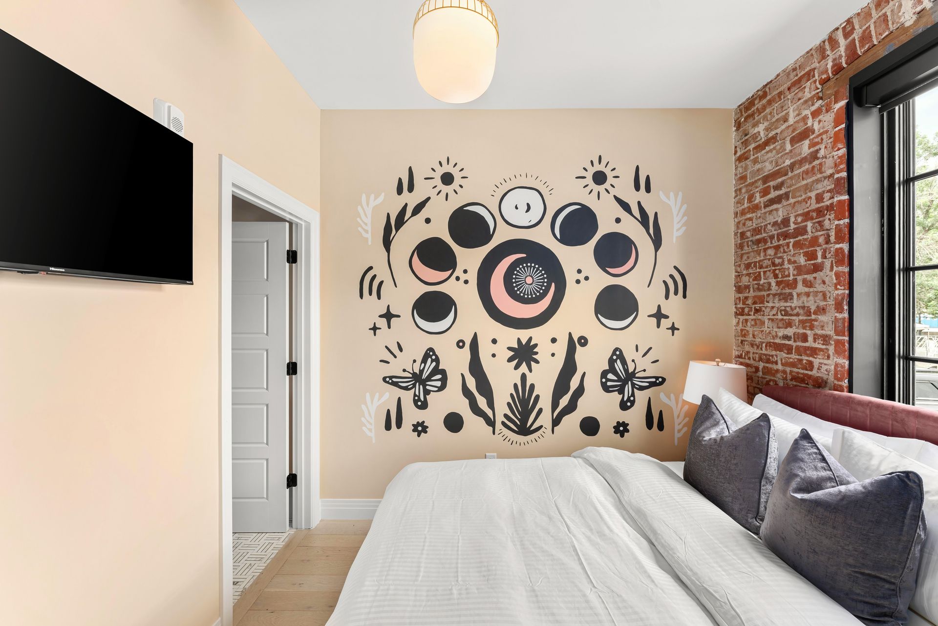 Modern bedroom with beige wall mural, bed, brick accent wall, window, and wall-mounted TV