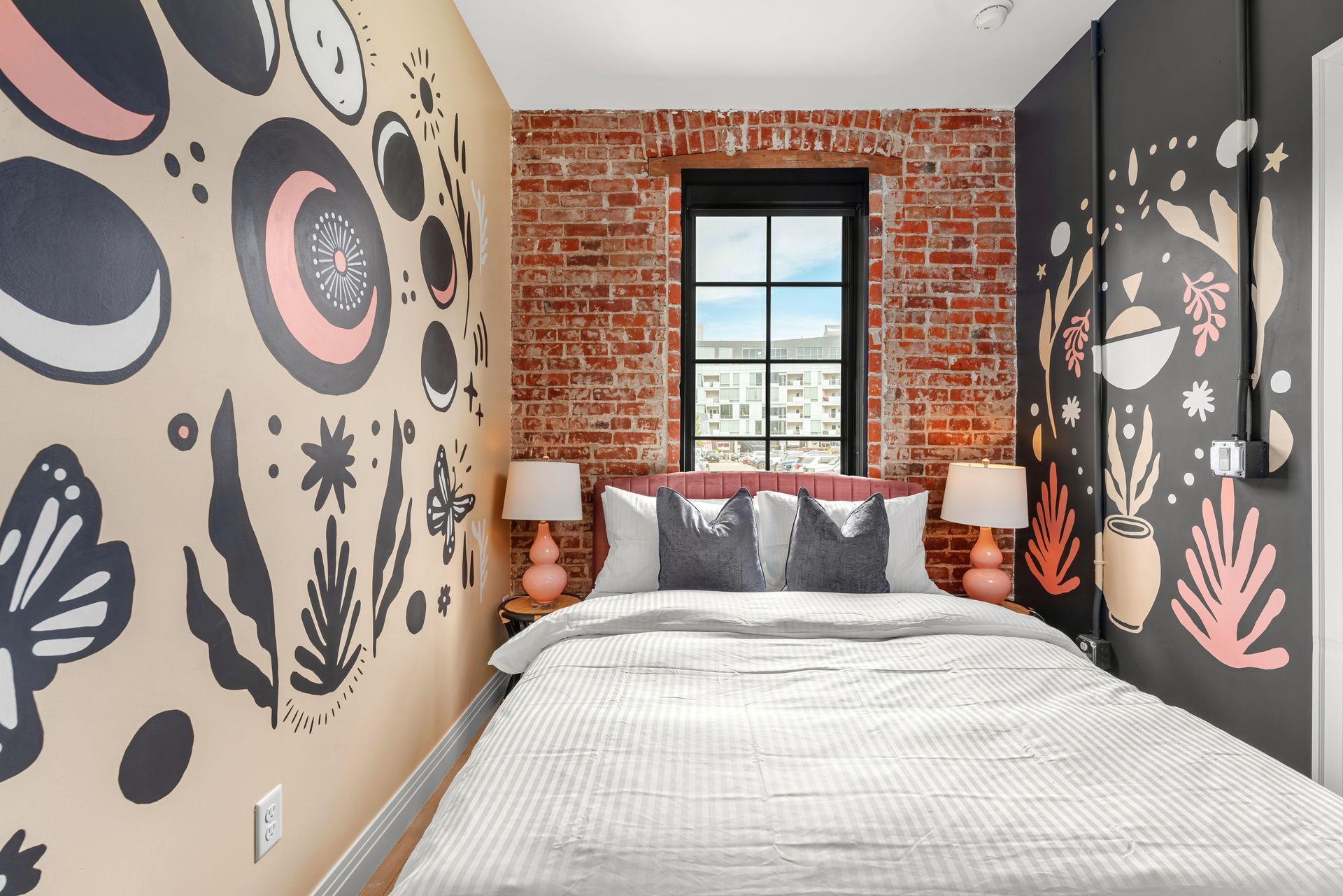 Small bedroom with brick accent wall, floral mural walls, and a neatly made bed by a window