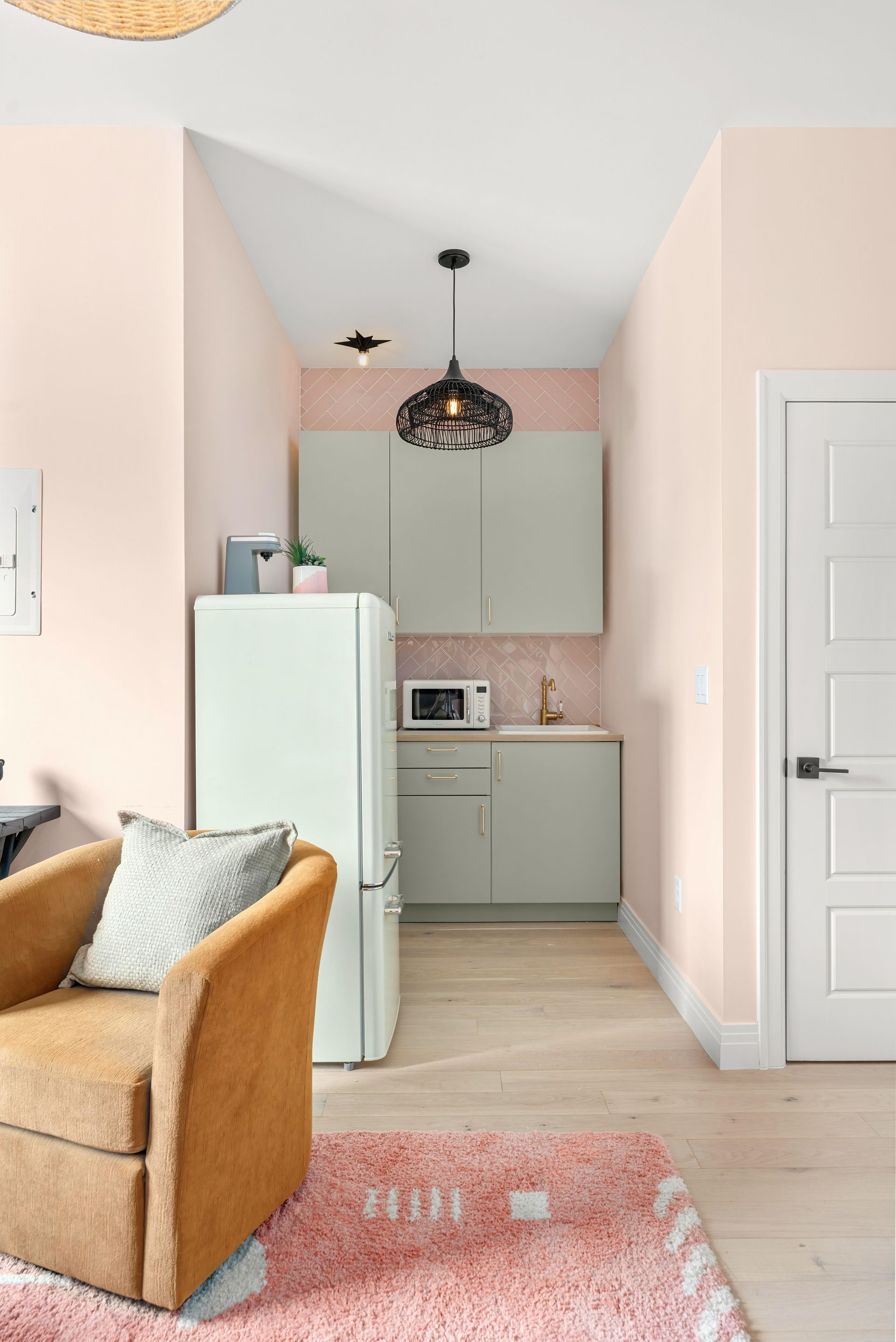 Small pastel kitchen nook with mint cabinets, white fridge, pink walls, and a black pendant light.