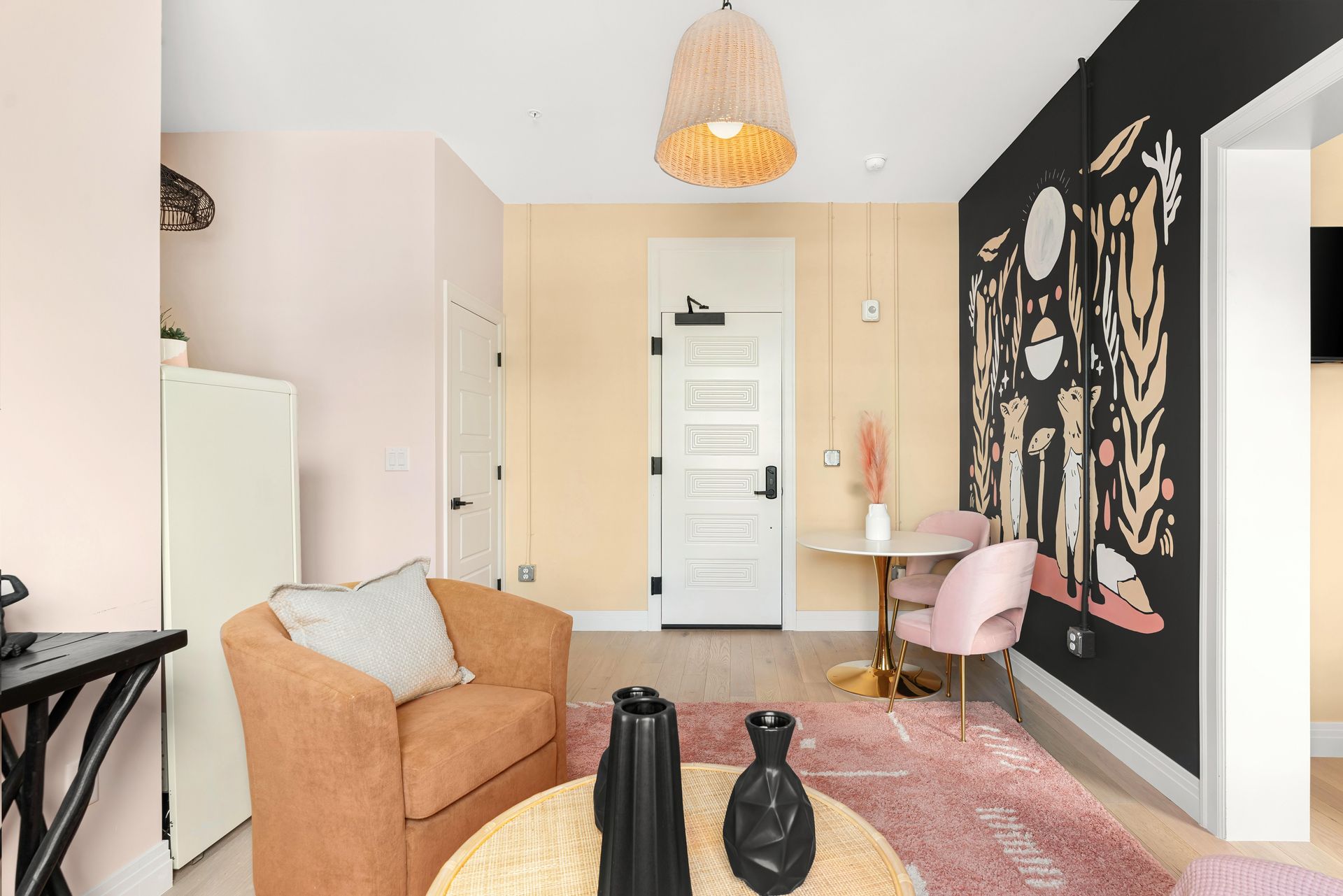 Cozy living room with tan chair, pink rug, black accent wall, and desk by a white door
