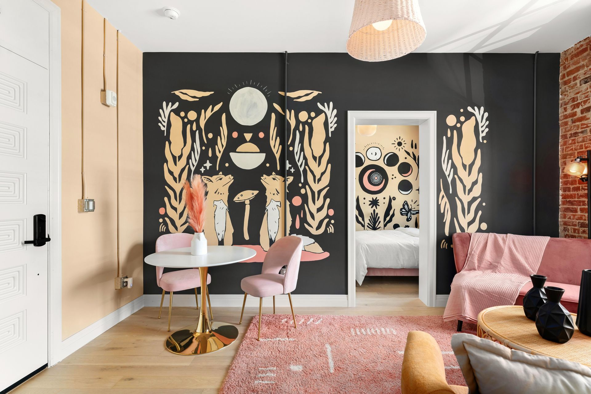 Stylish living room with black-and-gold mural wall, pink chairs, patterned rug, and white doorway
