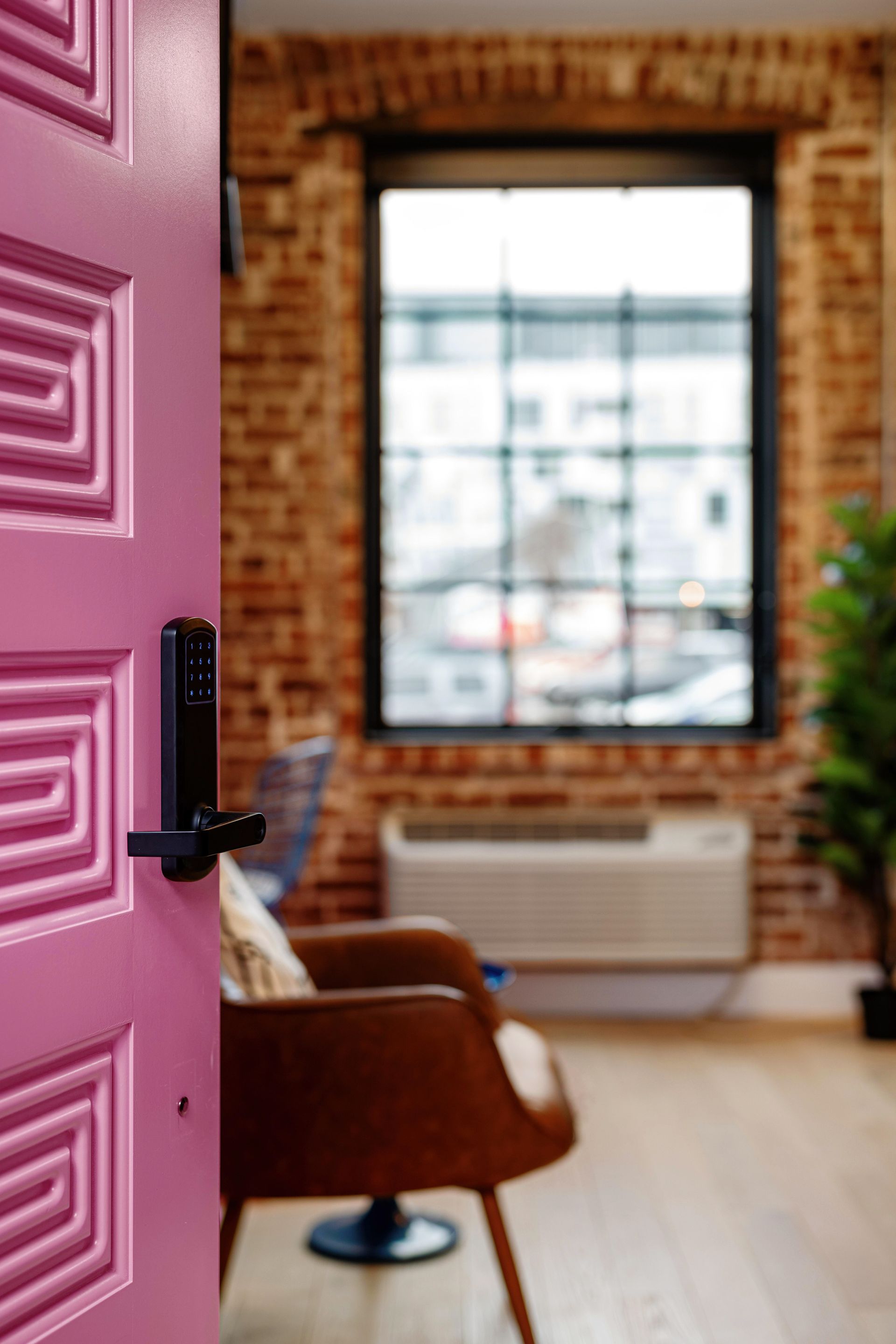 Pink door opening into a bright room with brick walls, a window, and a brown chair