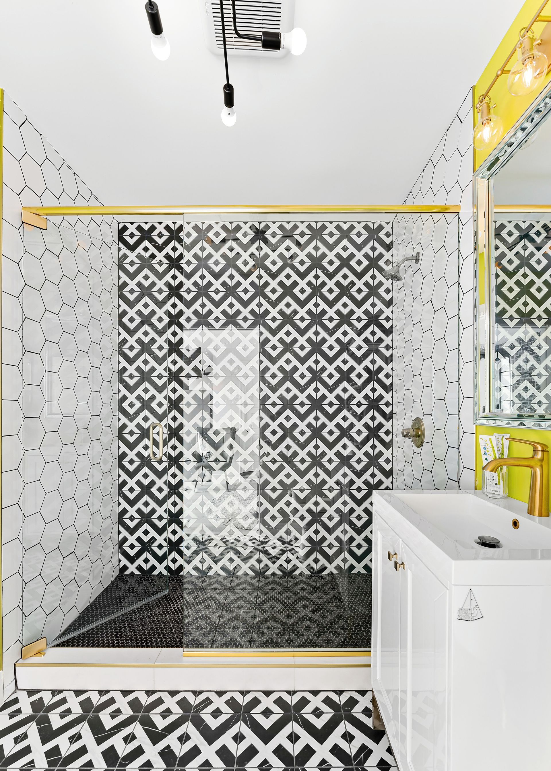 Modern bathroom shower with black-and-white patterned tile and a white vanity with yellow accents