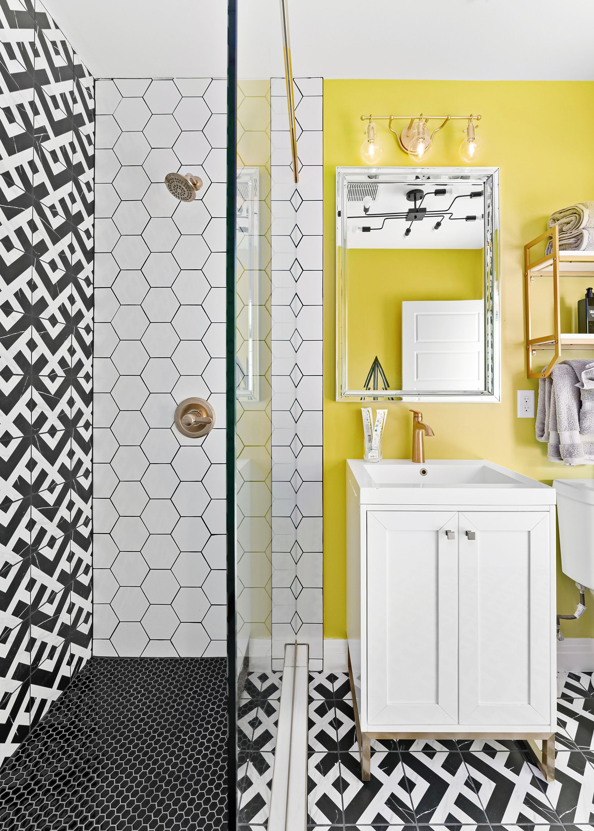 Colorful bathroom with yellow walls, white vanity, mosaic tile shower, and black-and-white geometric floor.