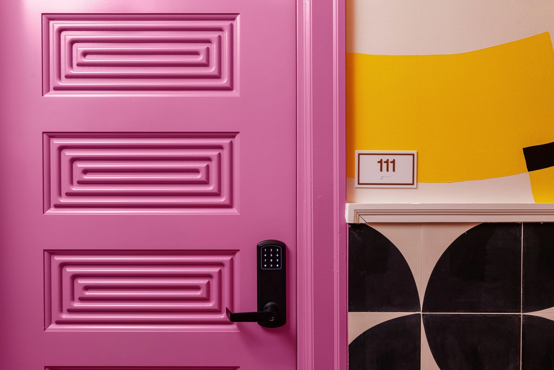 Pink paneled door with black handle beside yellow wall and black-and-white tiled corner