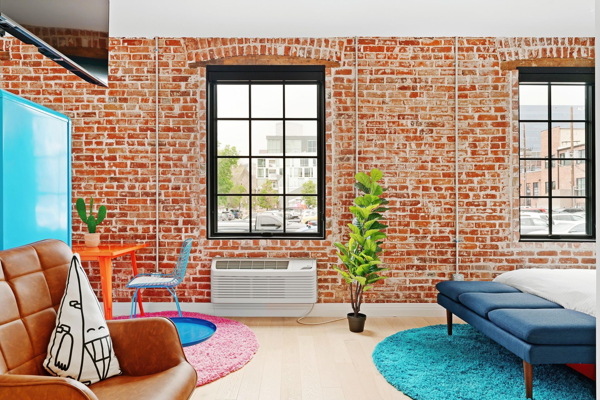 Bright loft living room with brick walls, large windows, blue sofa, tan chair, and colorful rugs