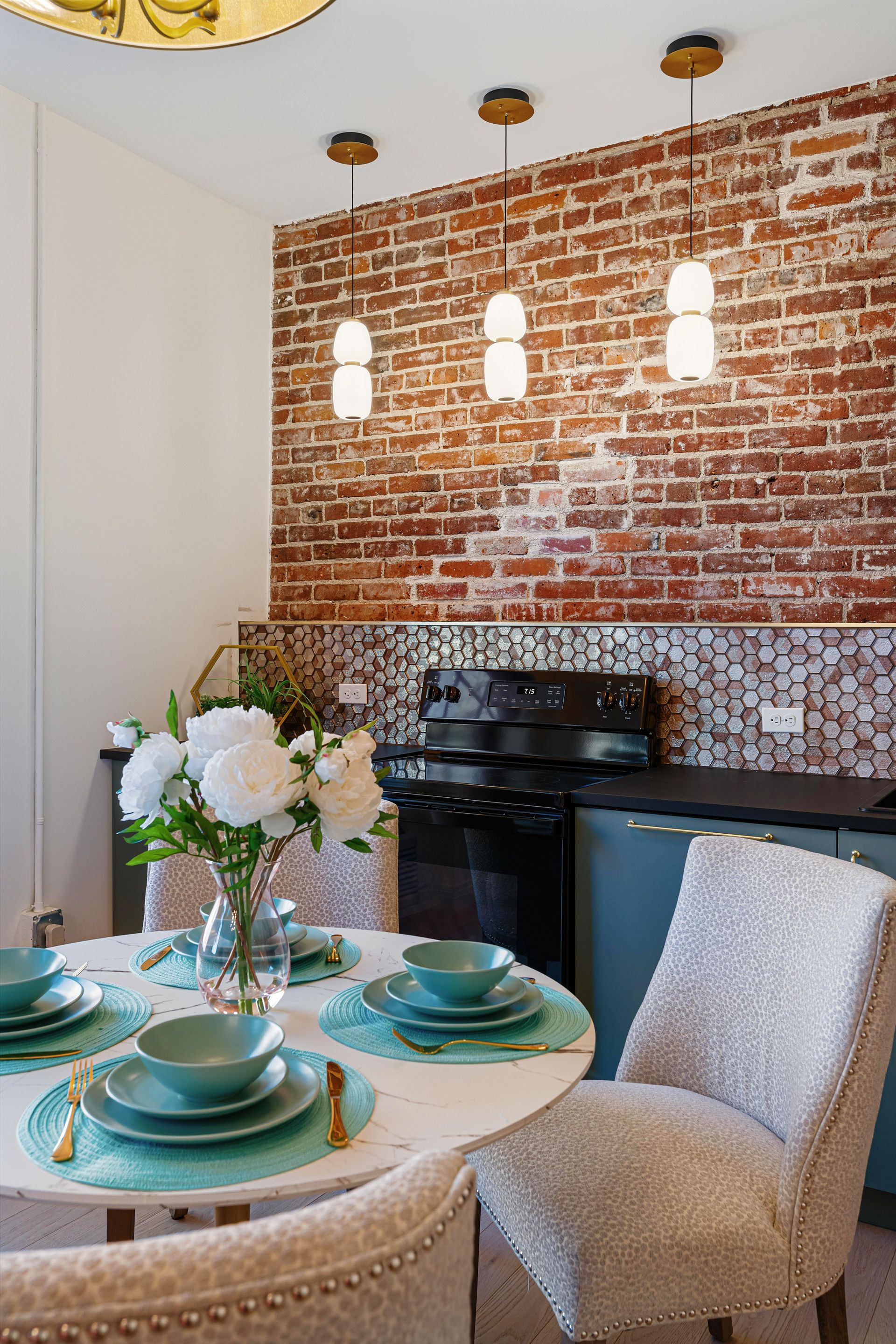 Cozy dining nook with exposed brick wall, round table set for four, and hanging pendant lights.
