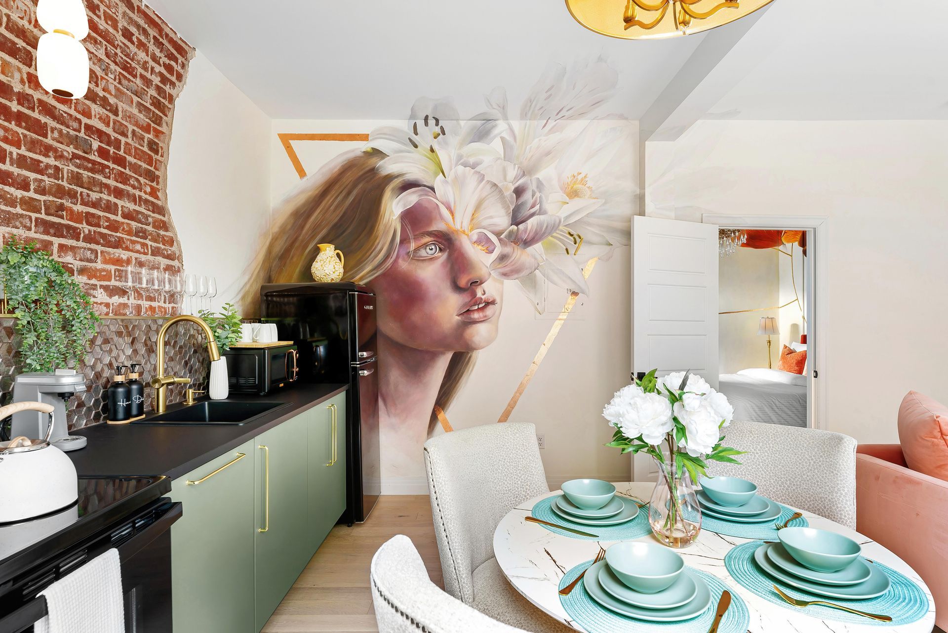 Bright kitchen-dining nook with mural portrait, black counter, green cabinets, and teal tableware.