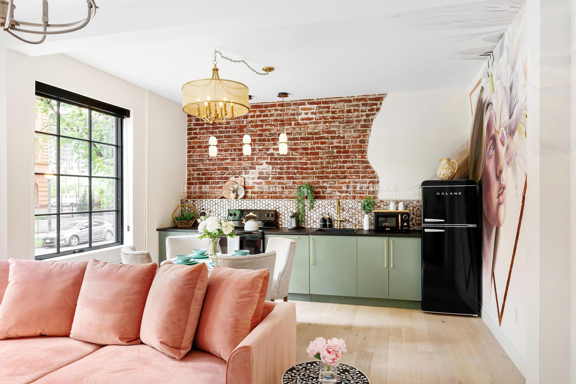 Bright living room with peach sofa, brick accent wall, green cabinets, and black fridge in open kitchen
