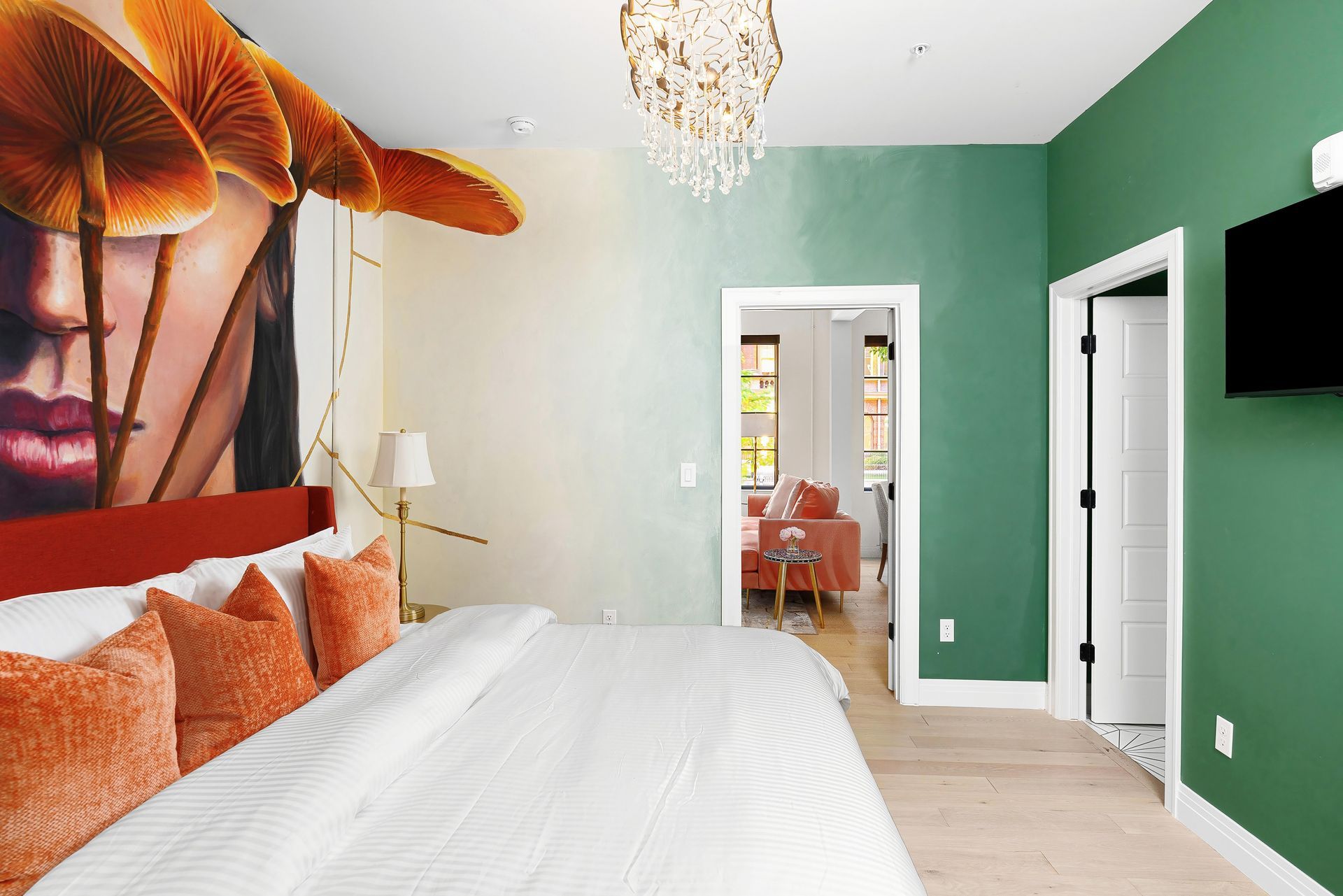 Modern bedroom with green walls, large floral mural, white bed, and doorway to a small sitting area