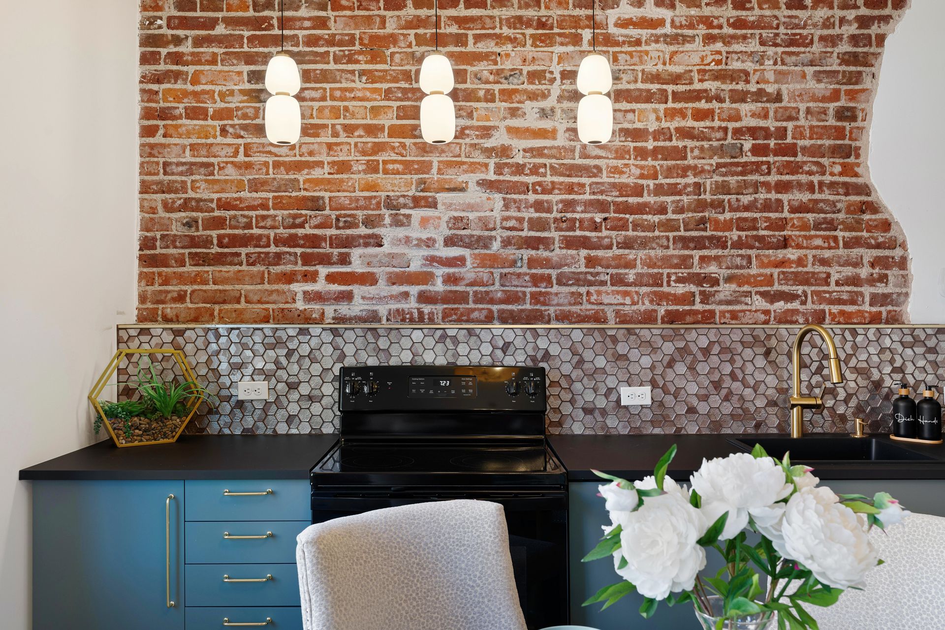 Modern kitchen with blue cabinets, black stove, exposed brick wall, and white flowers on the counter