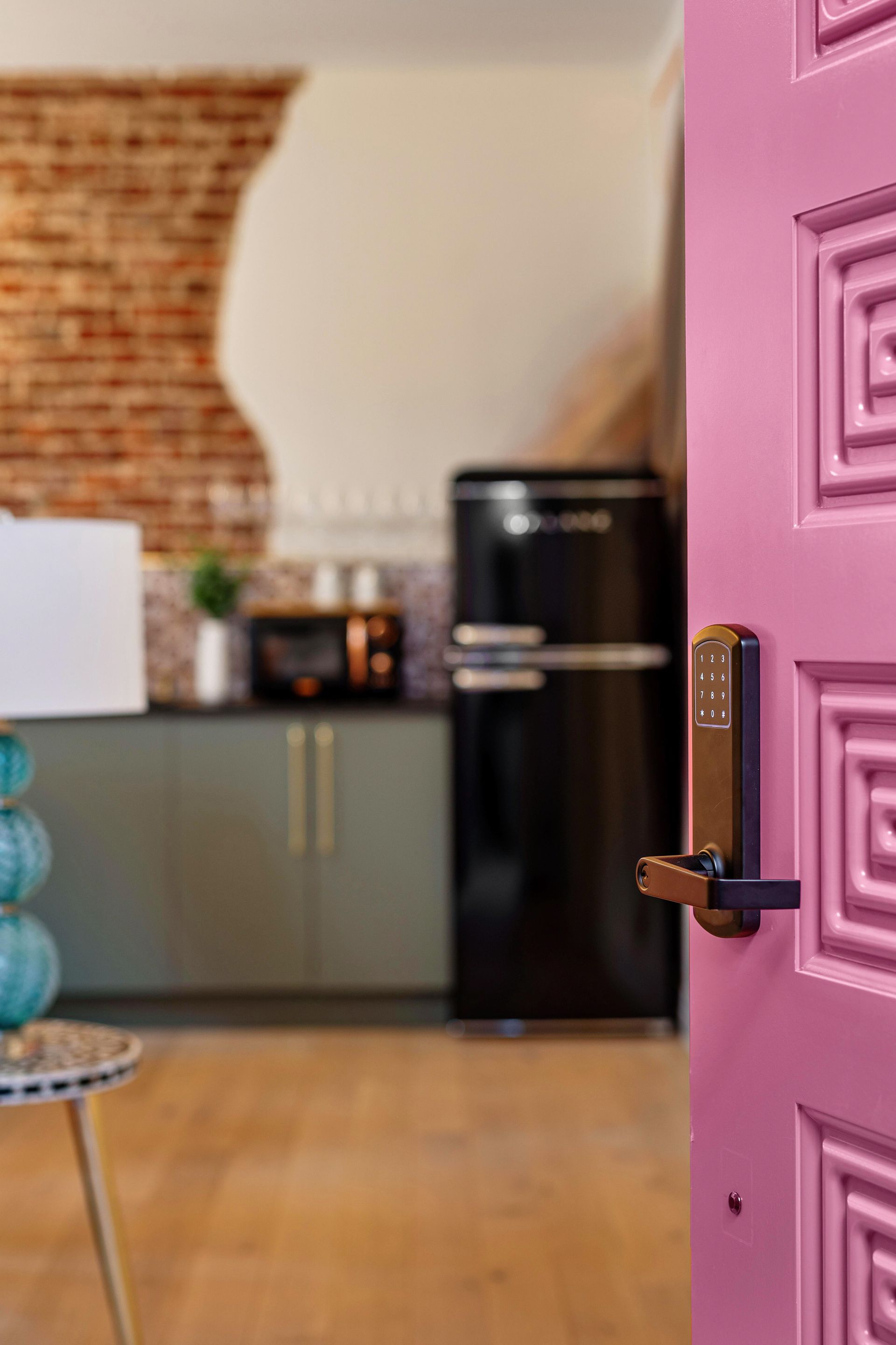 Open pink door to a cozy kitchen with wood floor, black fridge, and exposed brick wall