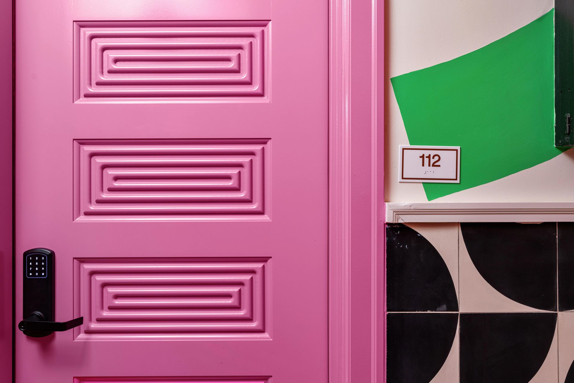 Pink door with black keypad lock beside a wall marked 112 and green geometric decor
