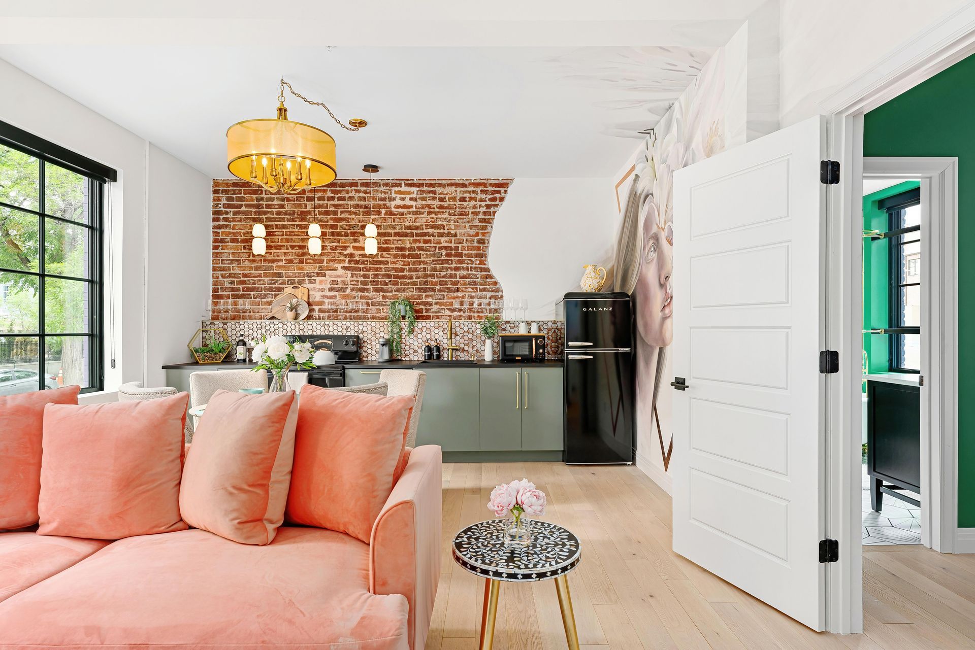 Bright living room with coral sofa, brick wall, open door, and green kitchen beyond