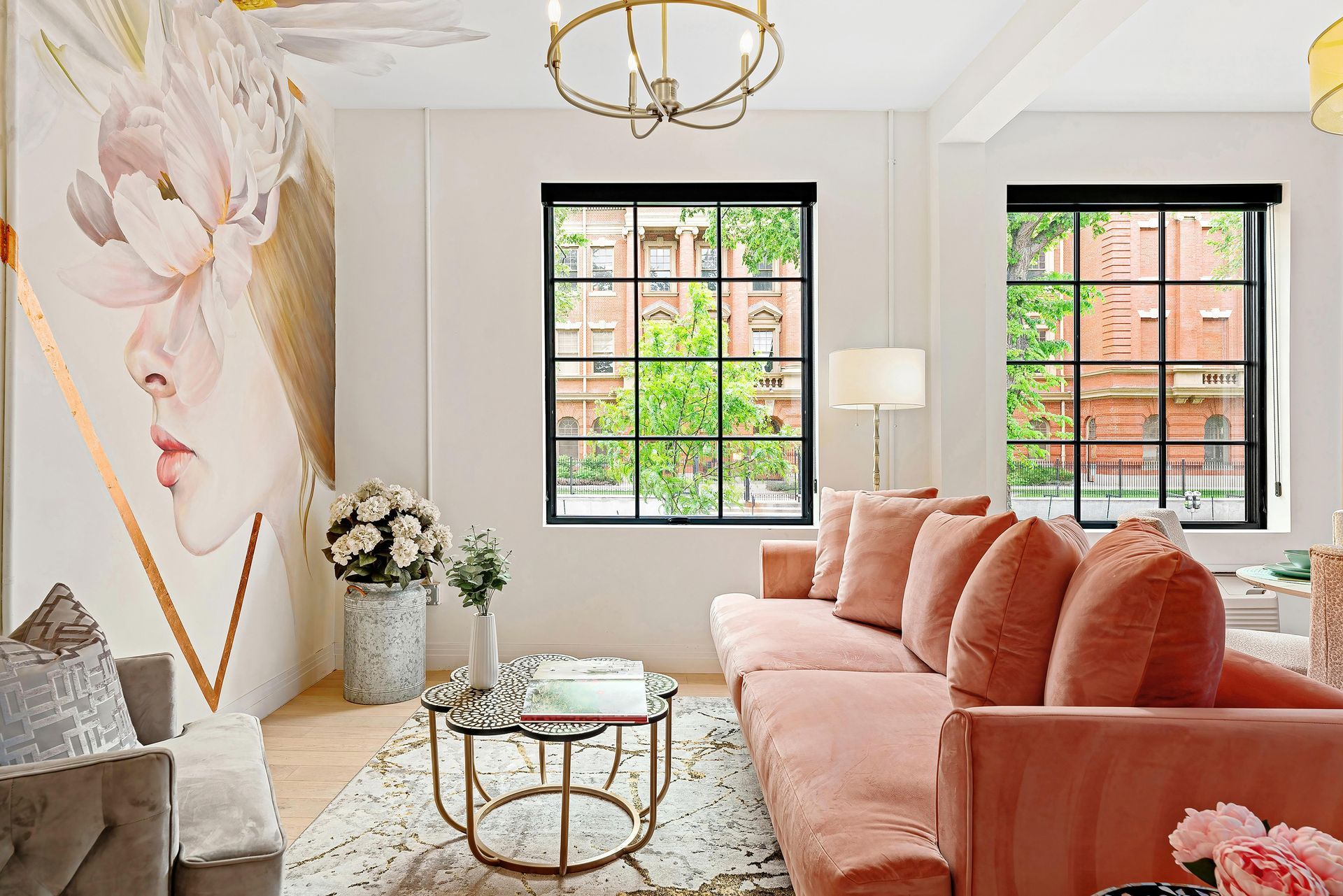 Bright living room with coral sofa, floral wall art, gold coffee table, and two black-framed windows