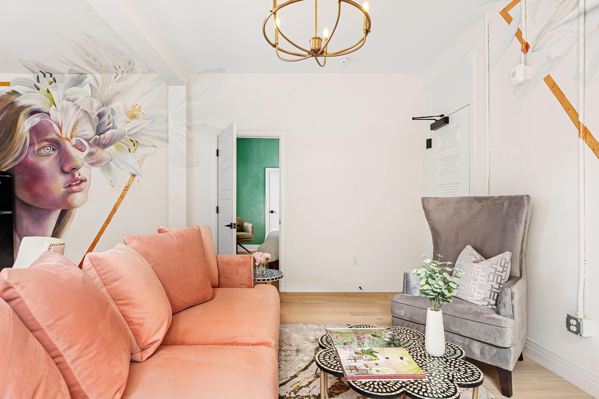 Bright living room with coral sofa, gray chair, gold chandelier, and large floral wall art