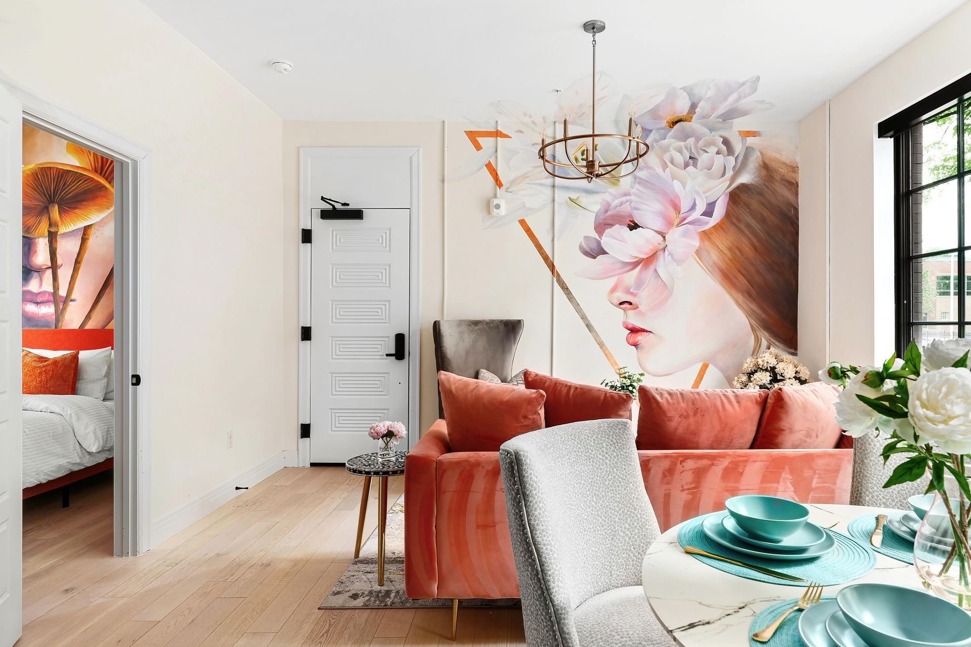 Modern living room with coral chairs, dining table, floral wall art, and large windows