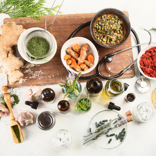 Assorted herbs, spices, oils, and kitchen tools arranged on a white table with a wooden board