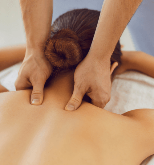 Massage therapist kneading a client's upper back and neck with hands on a spa table.
