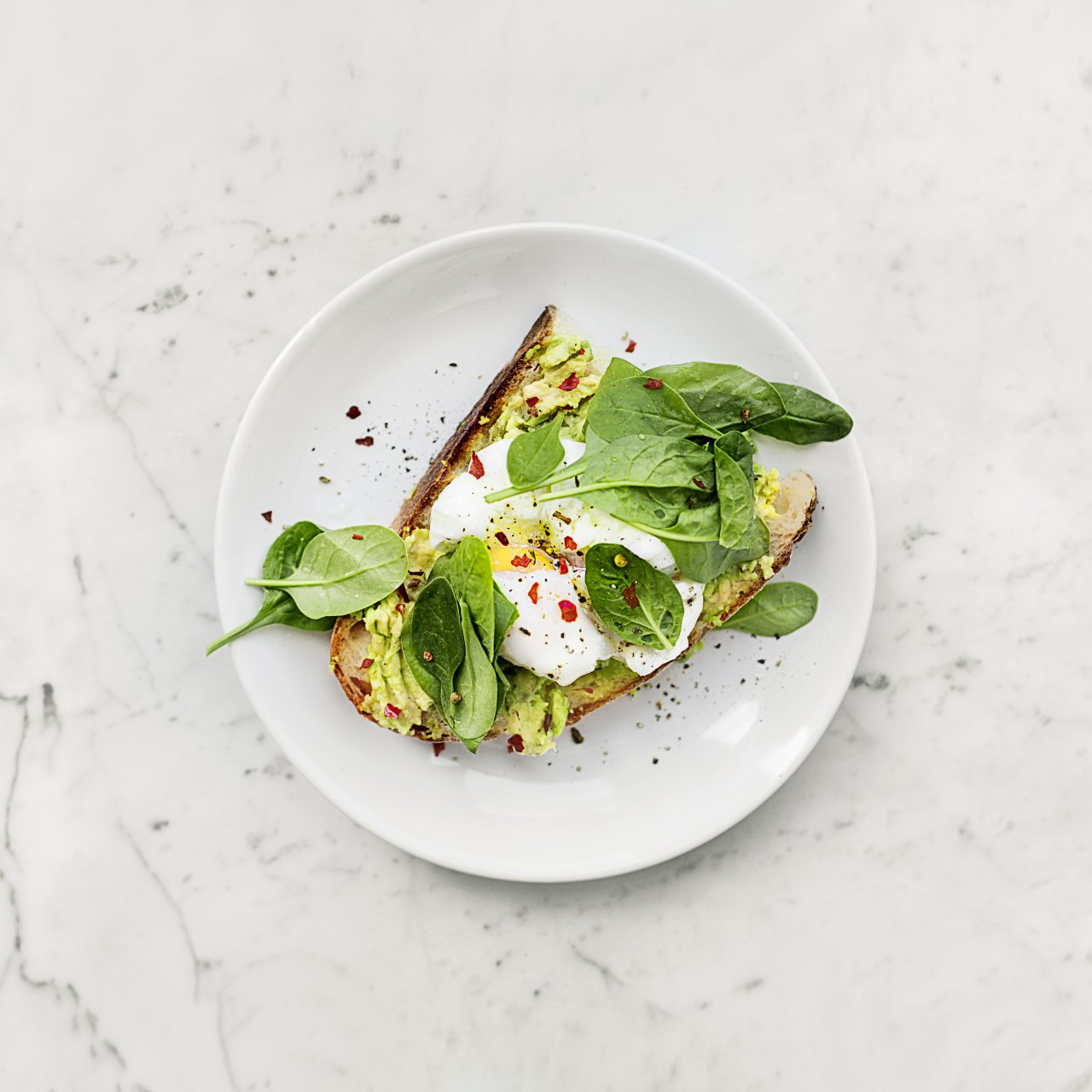Open-faced sandwich with greens and white cheese on a white plate, sprinkled with red pepper flakes.