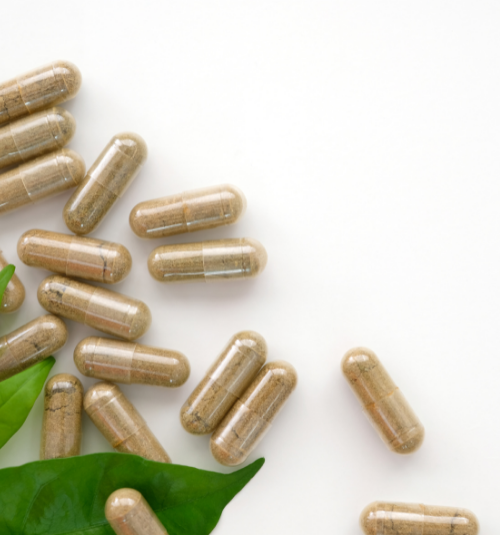 Clear capsules with beige powder scattered on a white surface with green leaves in the corner