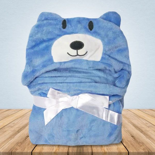 Op een houten tafel ligt een blauwe teddybeerdeken met een witte strik.