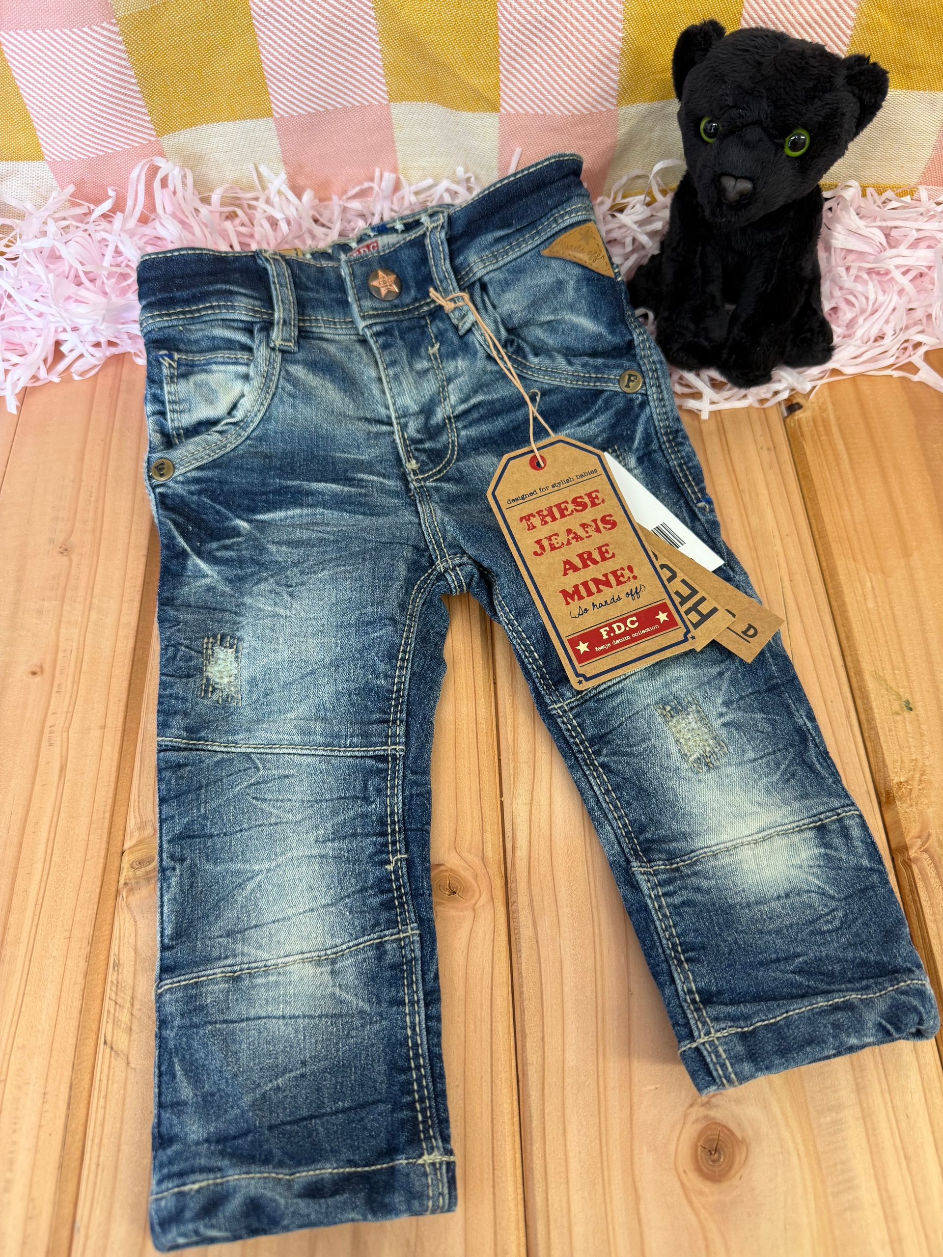 Er ligt een spijkerbroek op een houten tafel naast een knuffeldier.