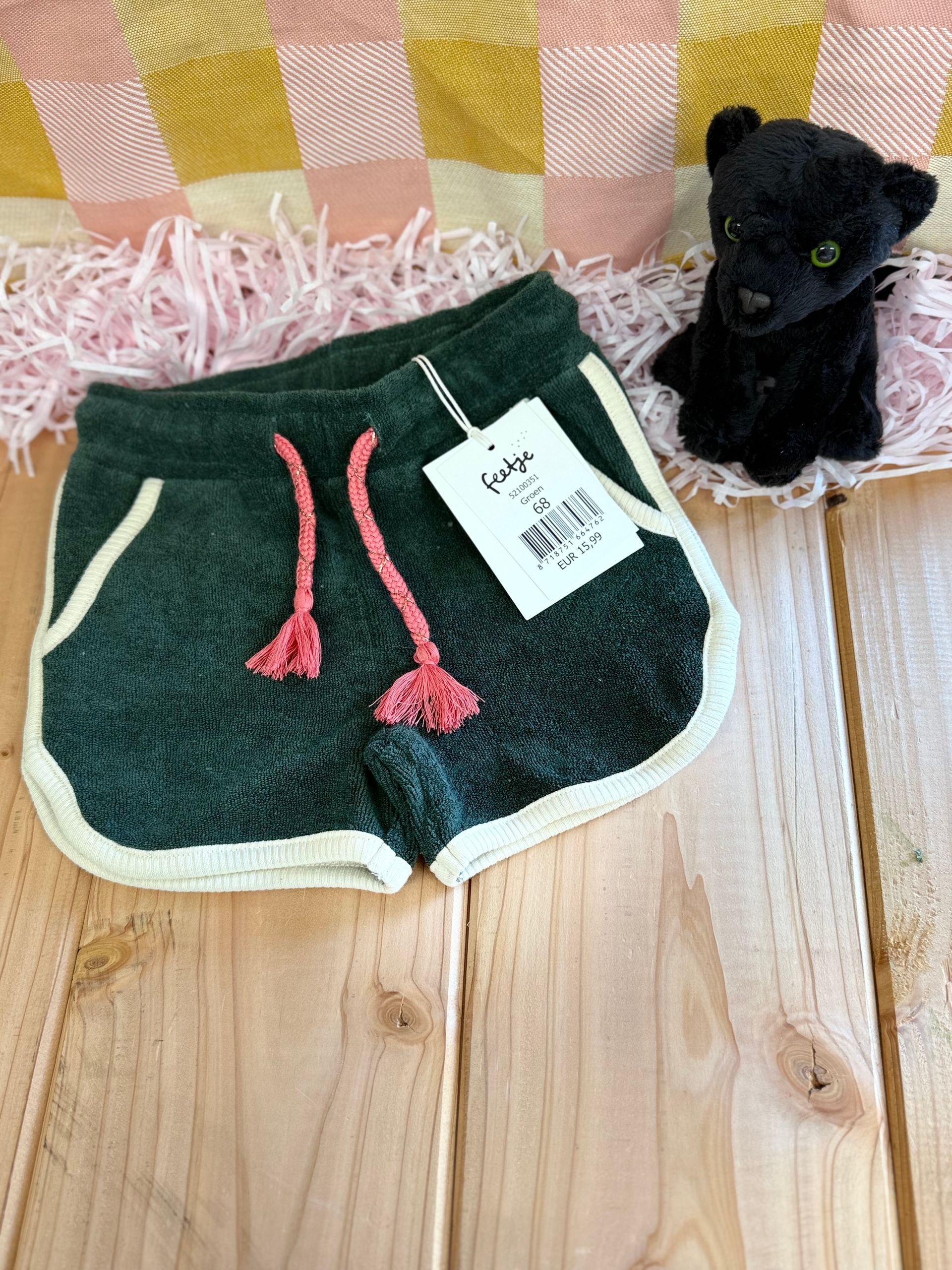 Een korte broek op een houten tafel naast een knuffeldier.