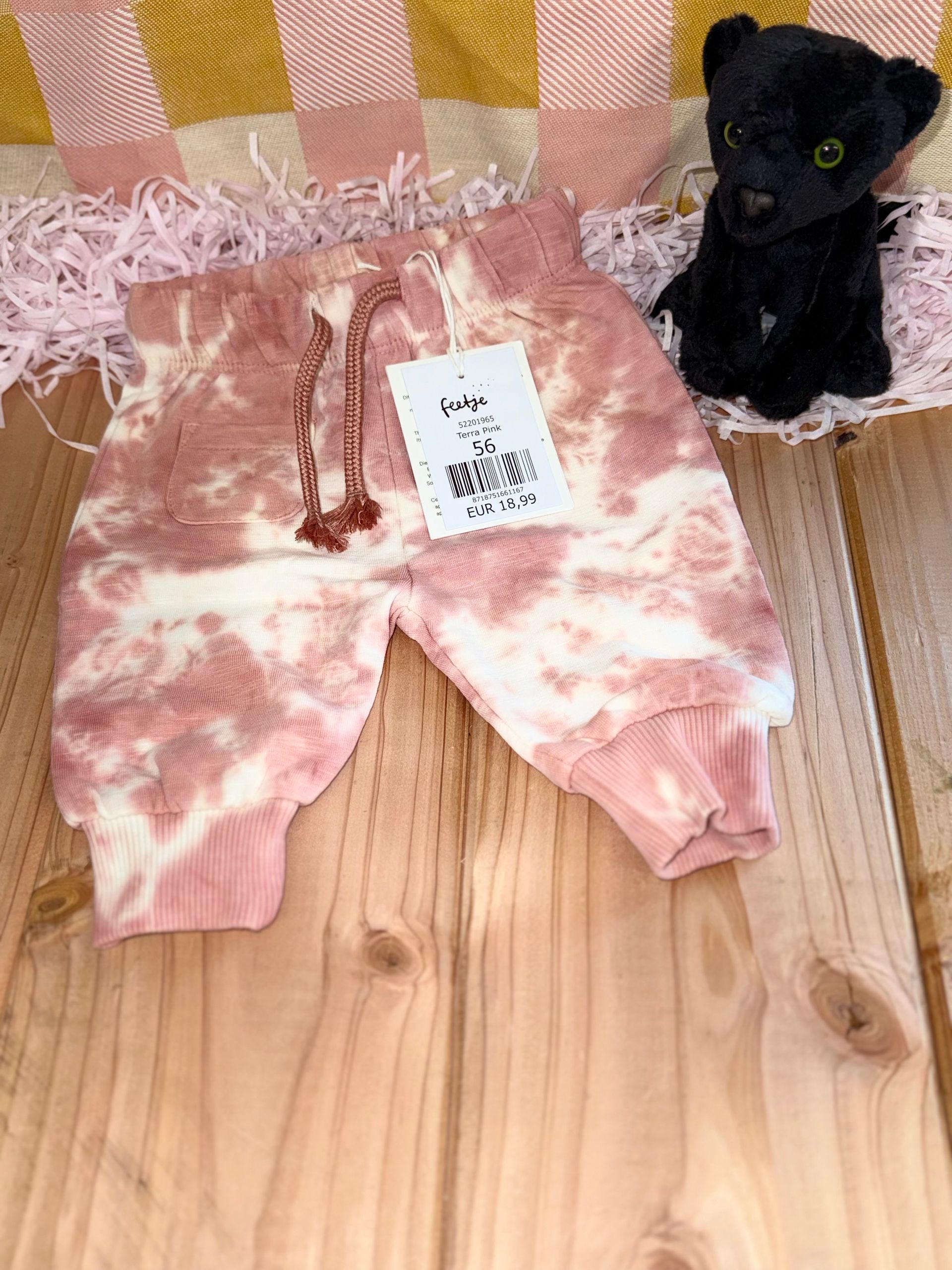 Een zwarte panter zit naast een tie-dye broek op een houten tafel.