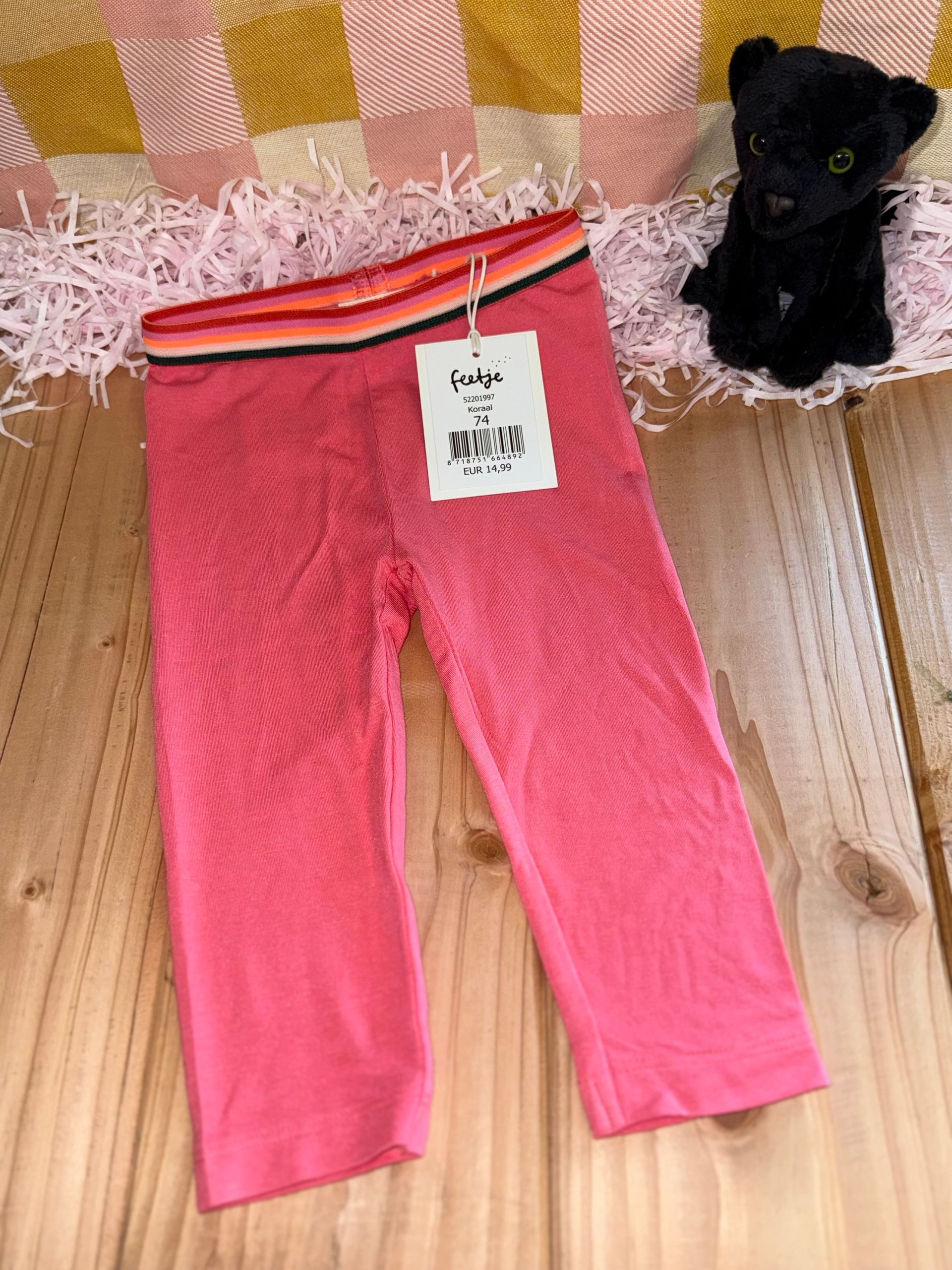 Op een houten tafel liggen een paar roze leggings naast een knuffeldier.
