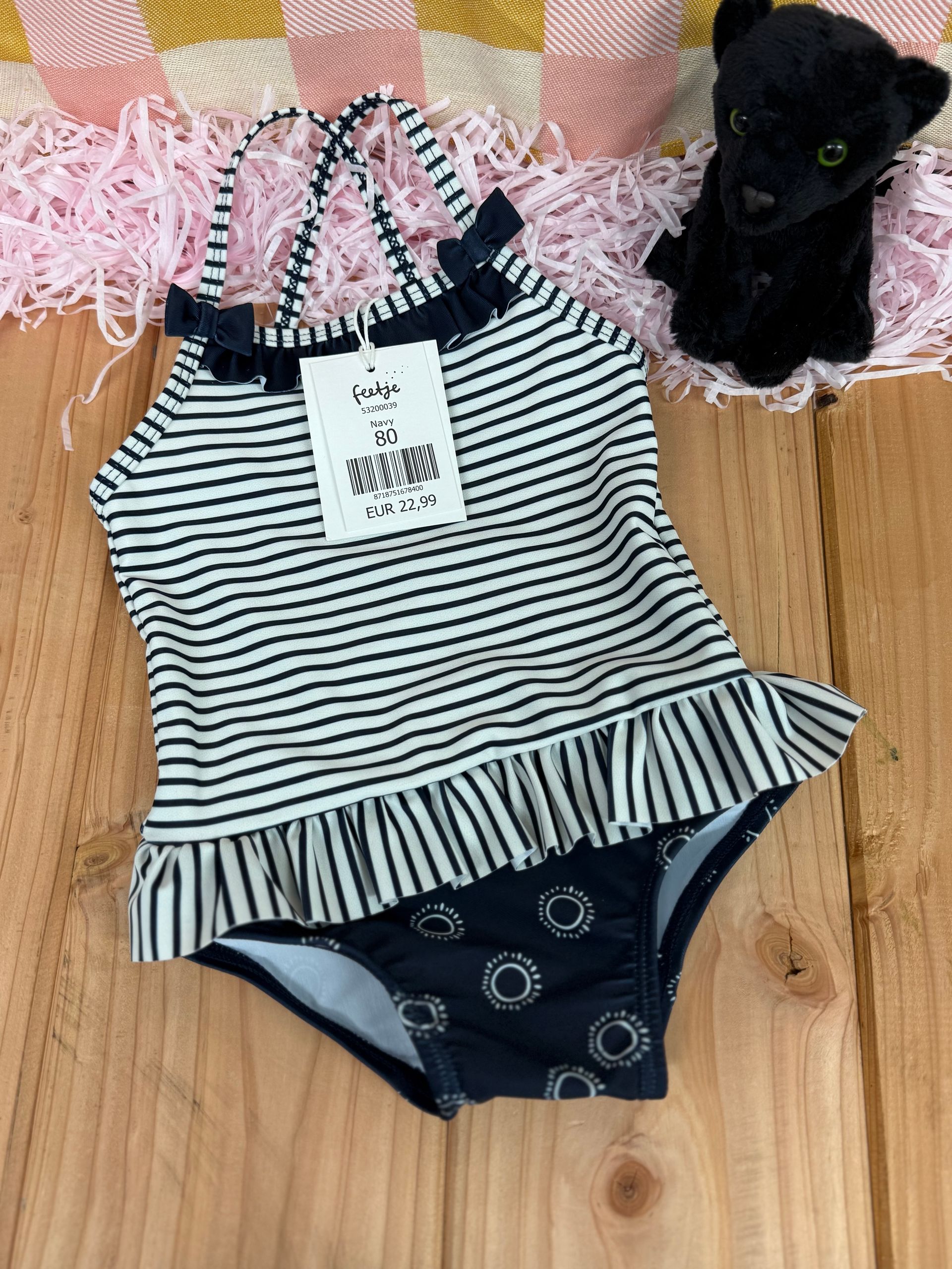 Een zwart-wit gestreept badpak ligt op een houten tafel naast een knuffeldier.