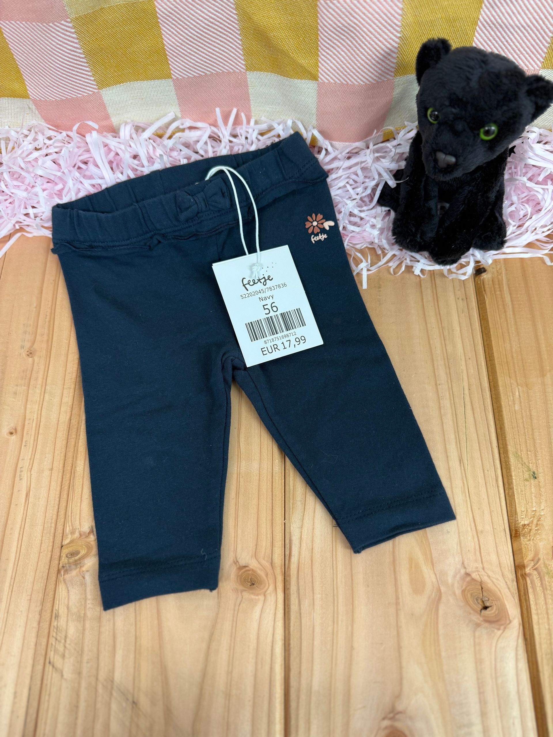 Een babybroekje ligt op een houten tafel naast een knuffeldier.