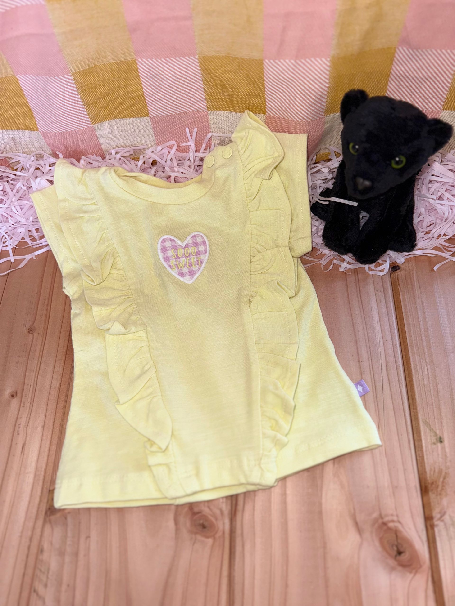 Een geel shirt ligt op een houten tafel naast een knuffeldier.