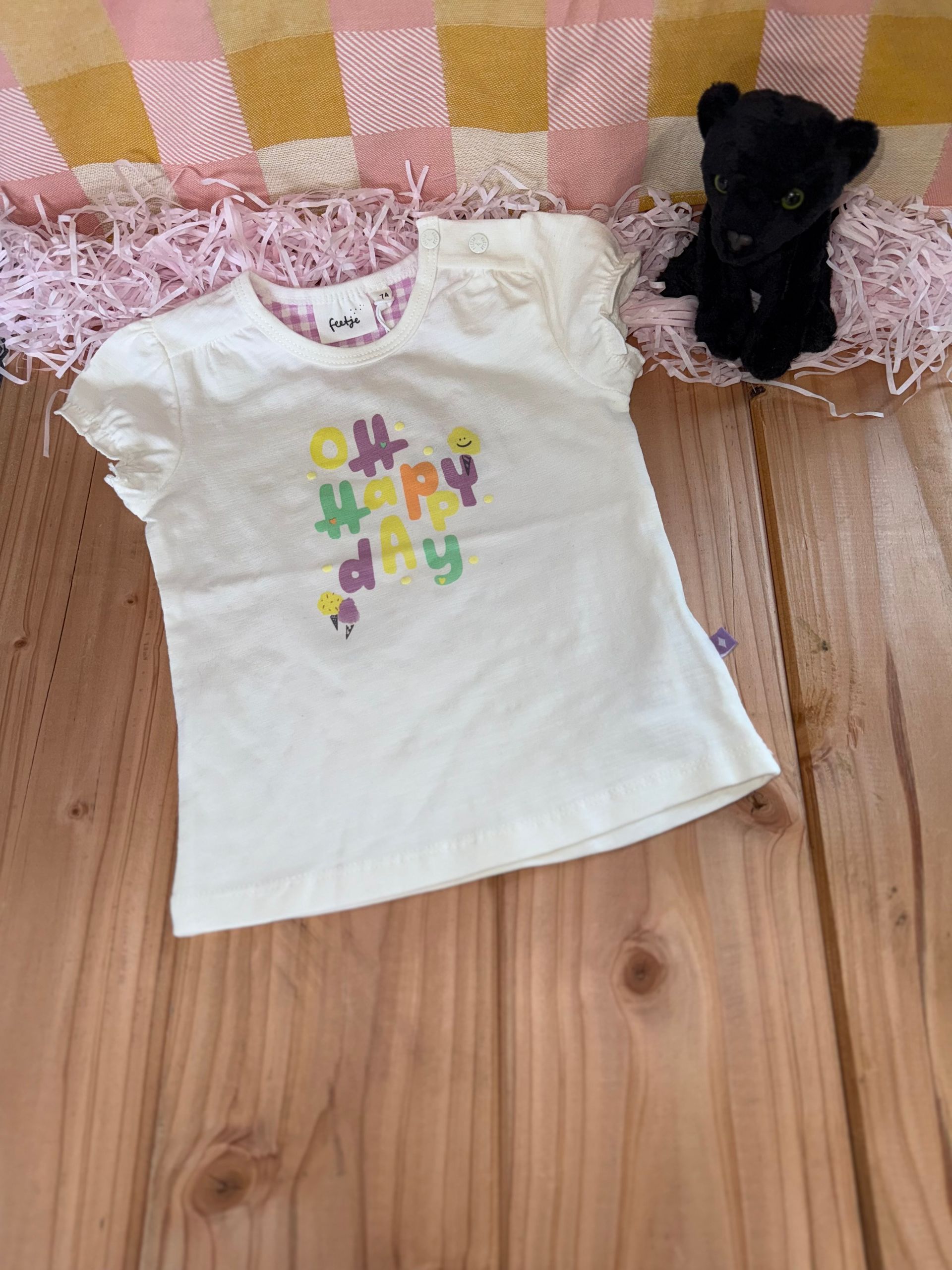 Een wit t-shirt ligt op een houten tafel naast een knuffeldier.