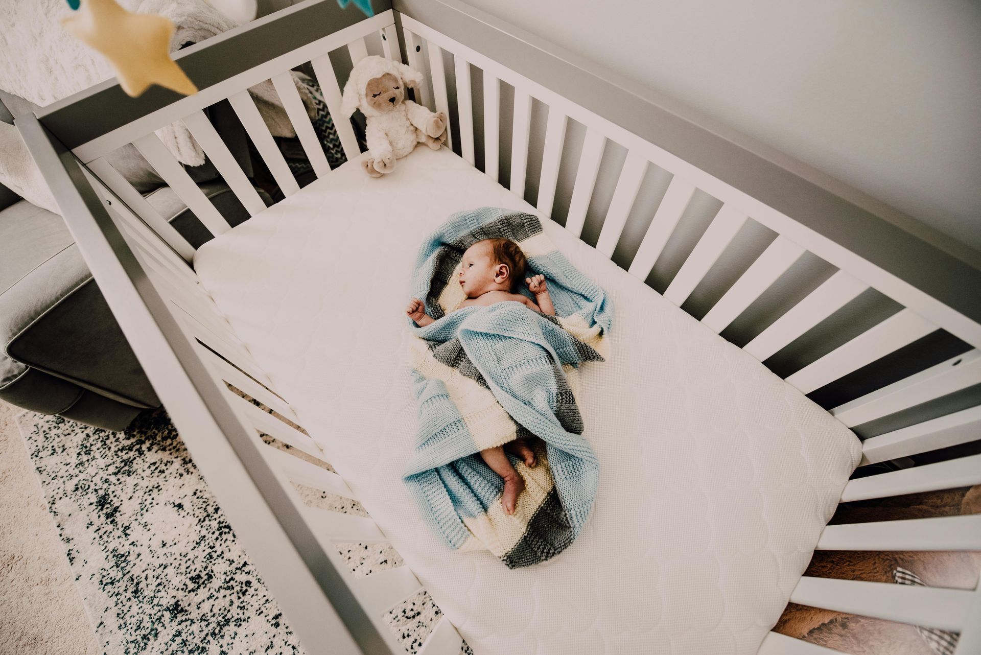 Een baby slaapt in een wiegje met een teddybeer.