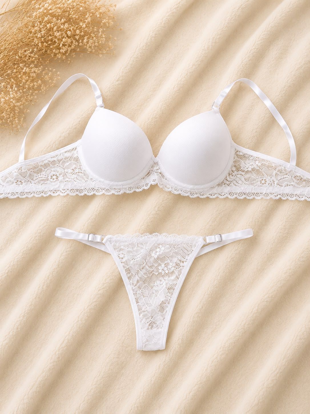 Conjunto de lencería de sujetador y tanga de encaje blanco sobre fondo de satén beige.