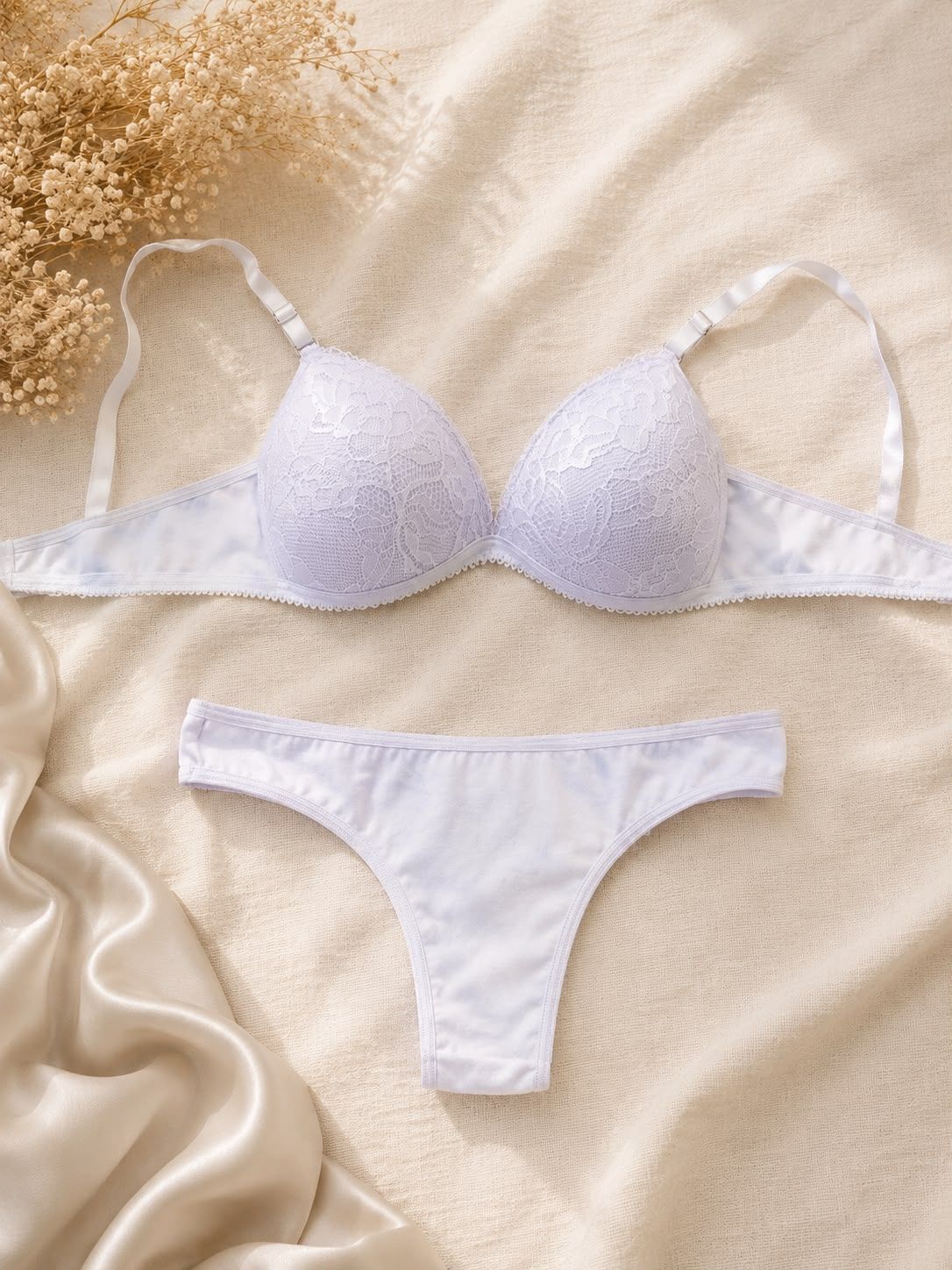 Conjunto de lencería de encaje blanco sobre un fondo de tela satinada color crema.