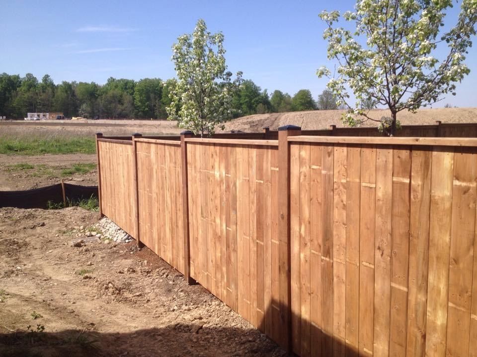 A wooden fence surrounds a dirt field with trees in the background built by Ironside Construction