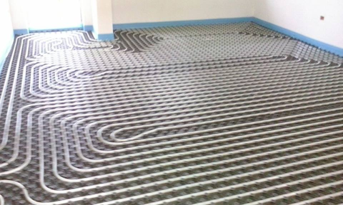 Tubi per riscaldamento a pavimento radiante posati in una stanza in costruzione, con porta e pareti bianche
