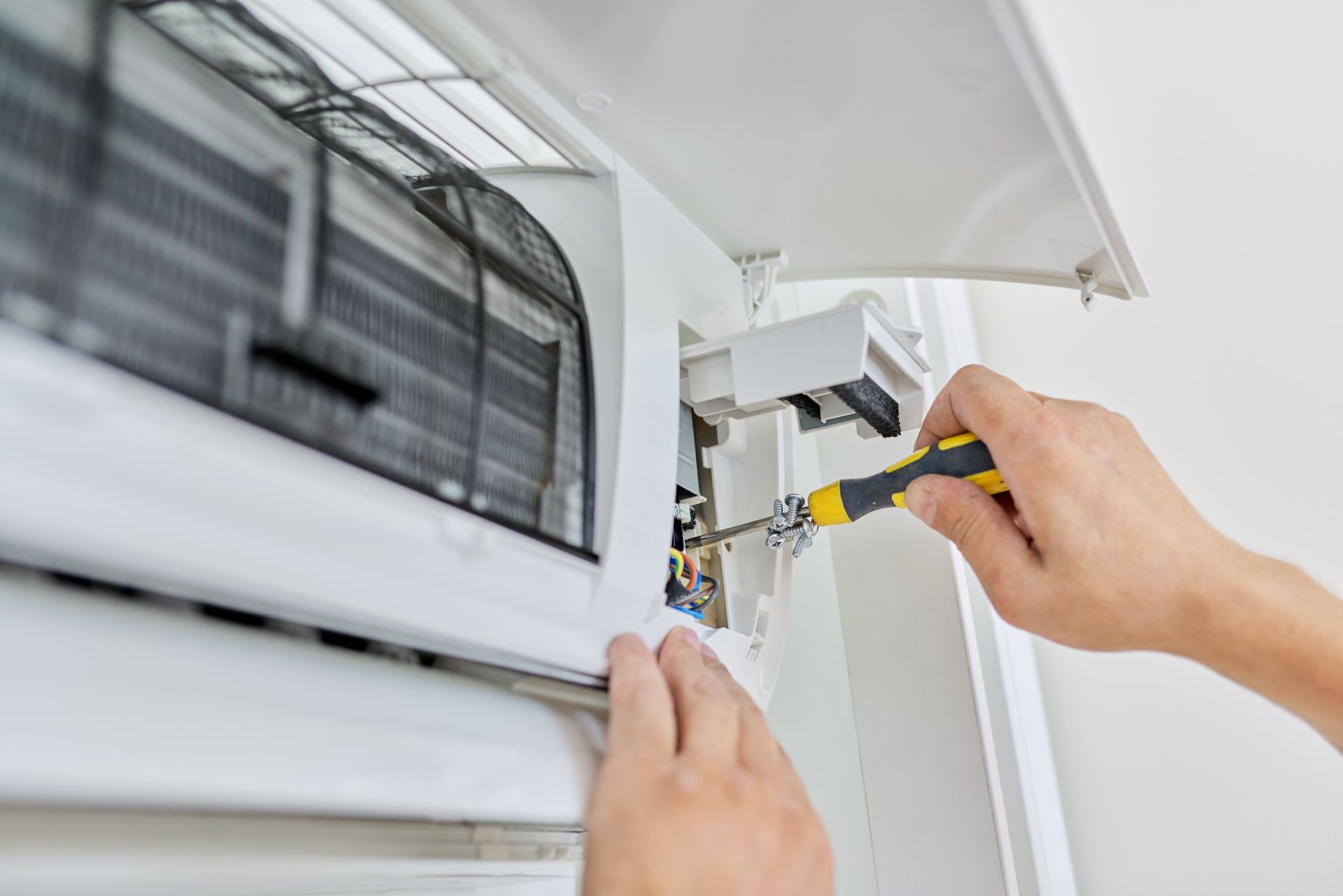Mani che stringono un'unità di condizionamento dell'aria con un cacciavite in un interno bianco.