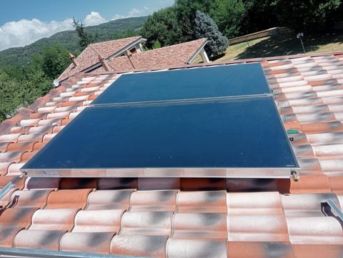 Pannelli solari per il riscaldamento dell'acqua su un tetto di tegole con le montagne sullo sfondo.